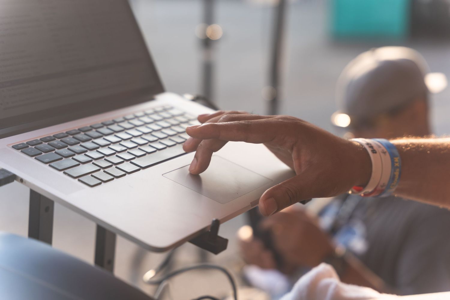 Hands typing on a silver laptop keyboard at an outdoor event.