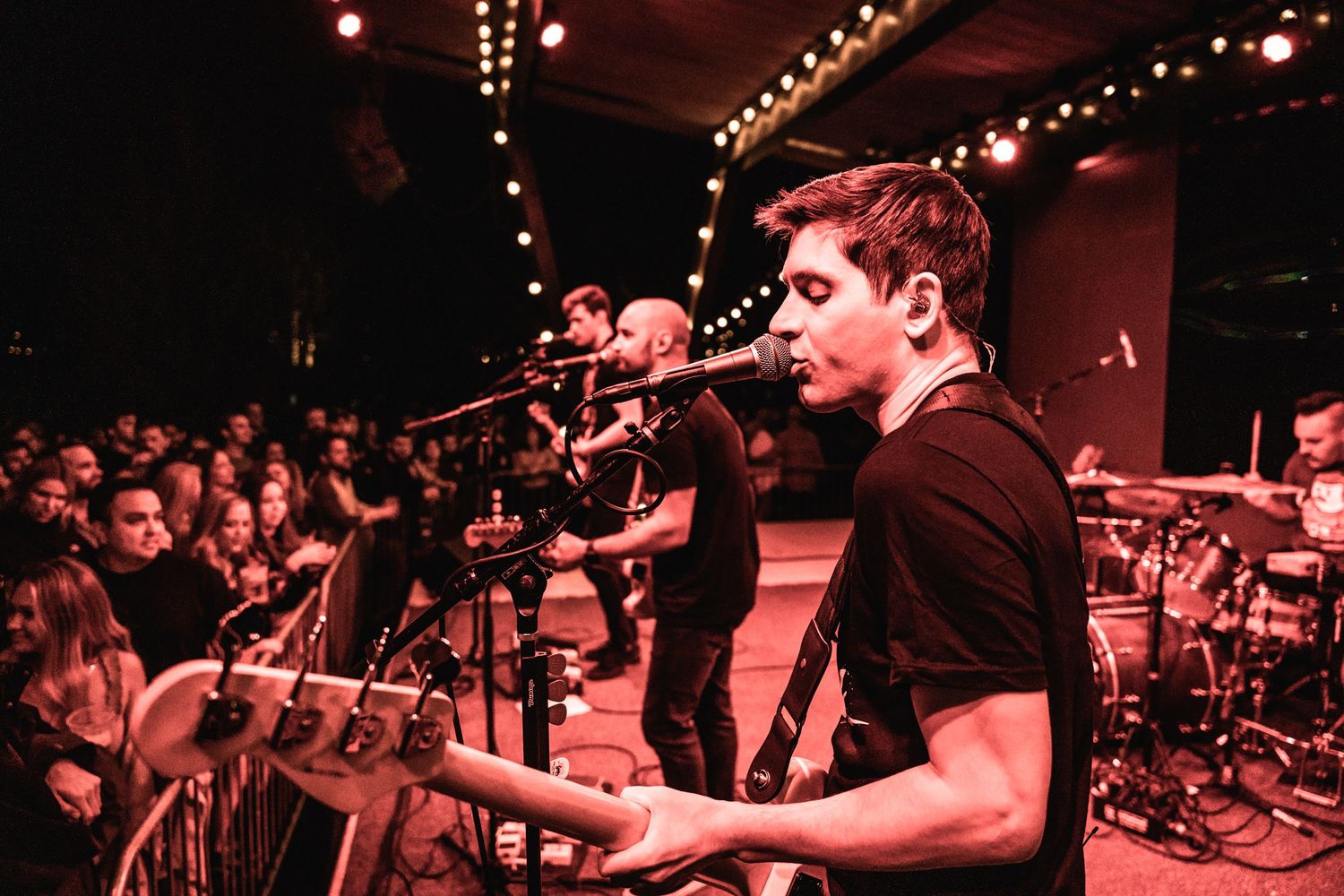 Musicians perform on dimly lit stage with red lighting and crowd visible.