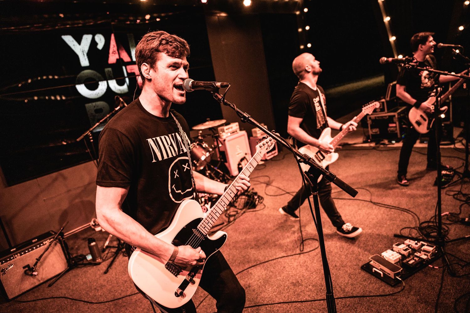 Musicians performing energetically on stage with guitars and microphones.