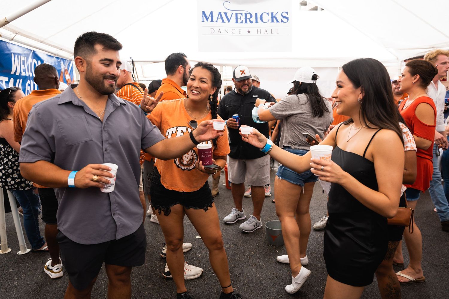 Groups of friends chatting and drinking at an outdoor party with Mavericks branding visible.