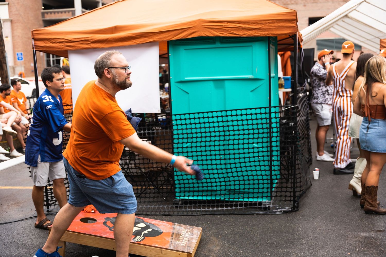 Person in orange shirt plays carnival game at outdoor event.