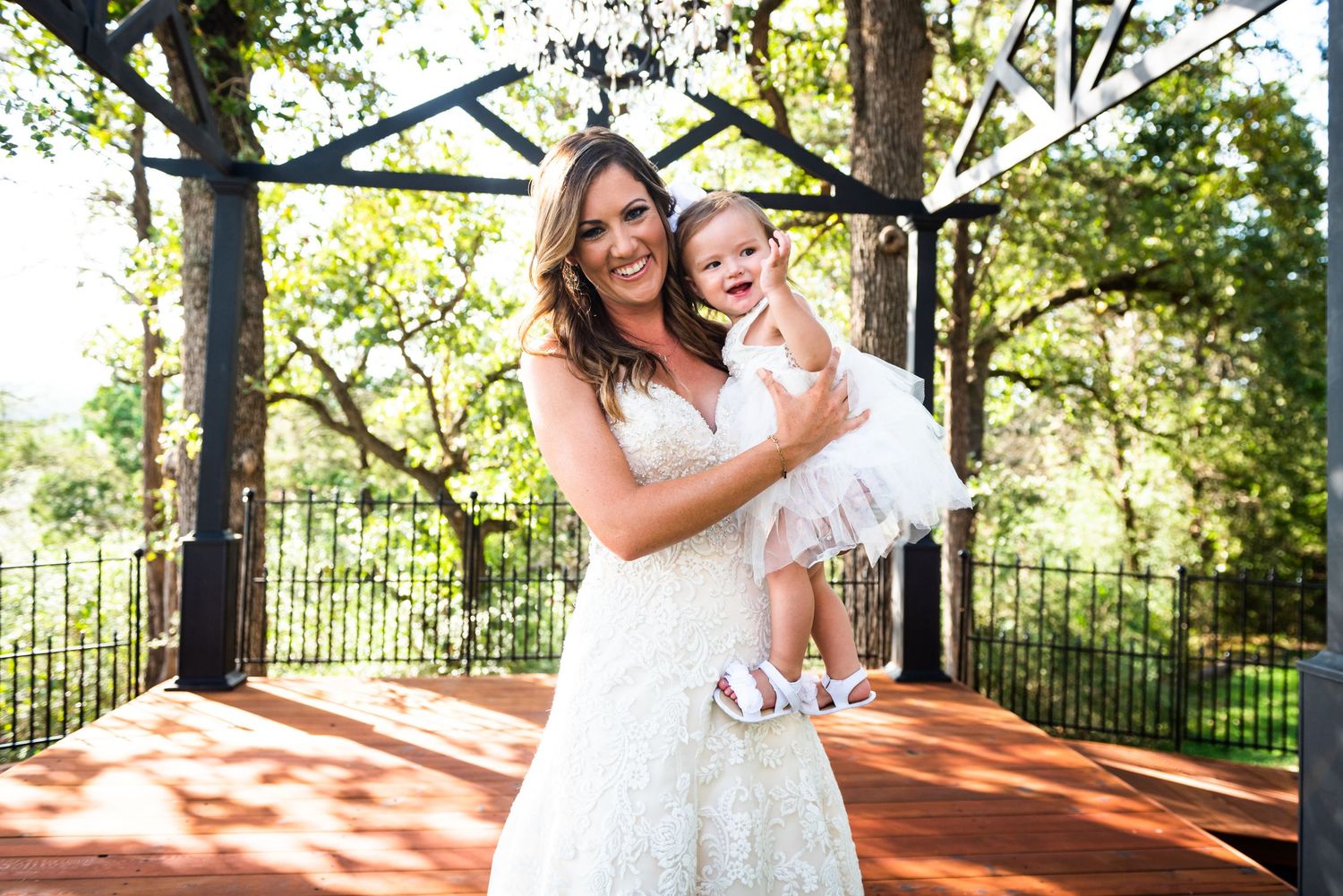 A joyful outdoor moment in white lace dress on a garden patio beneath trees.