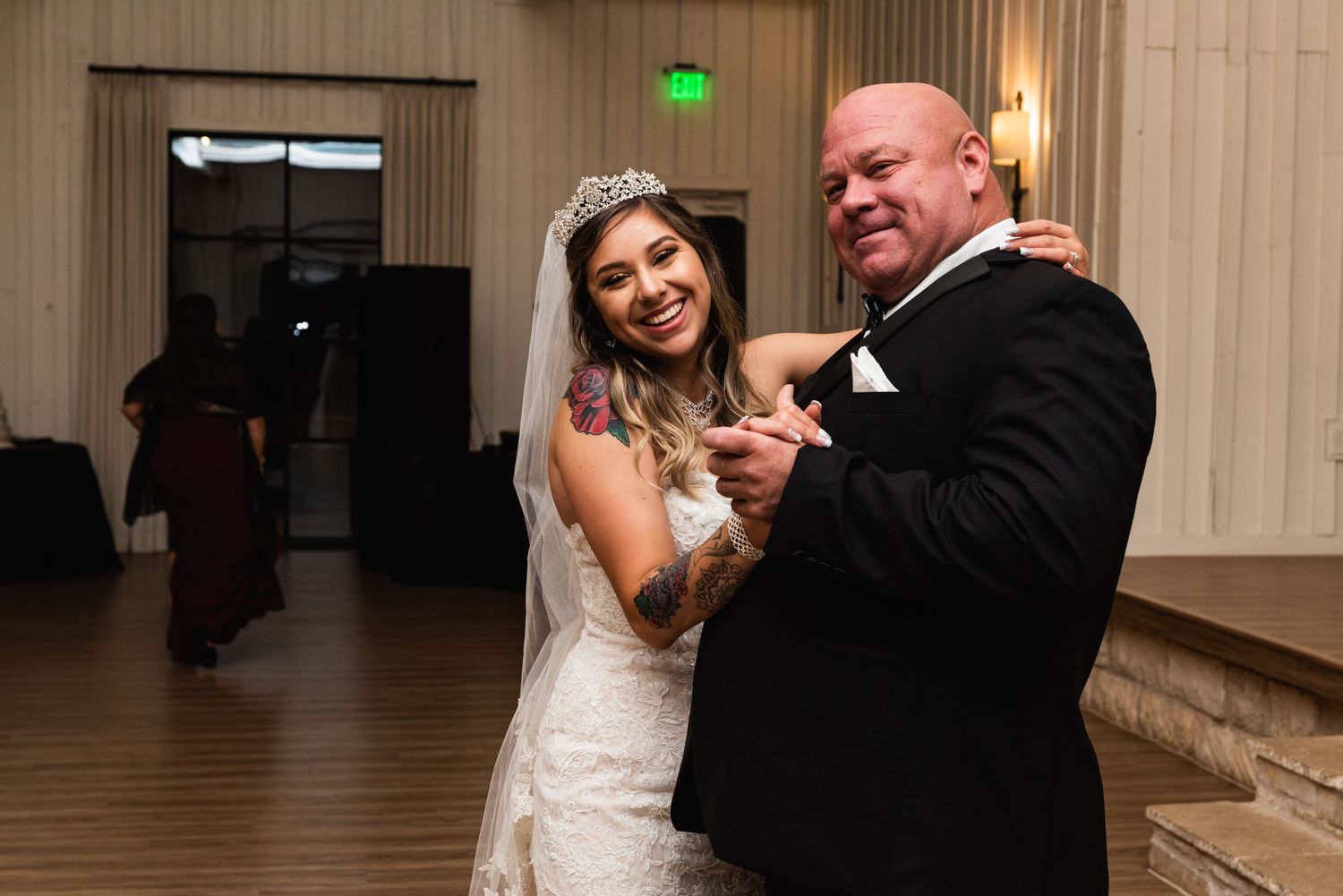 A couple shares their first dance as newlyweds in a beautifully lit reception hall with wood floors.