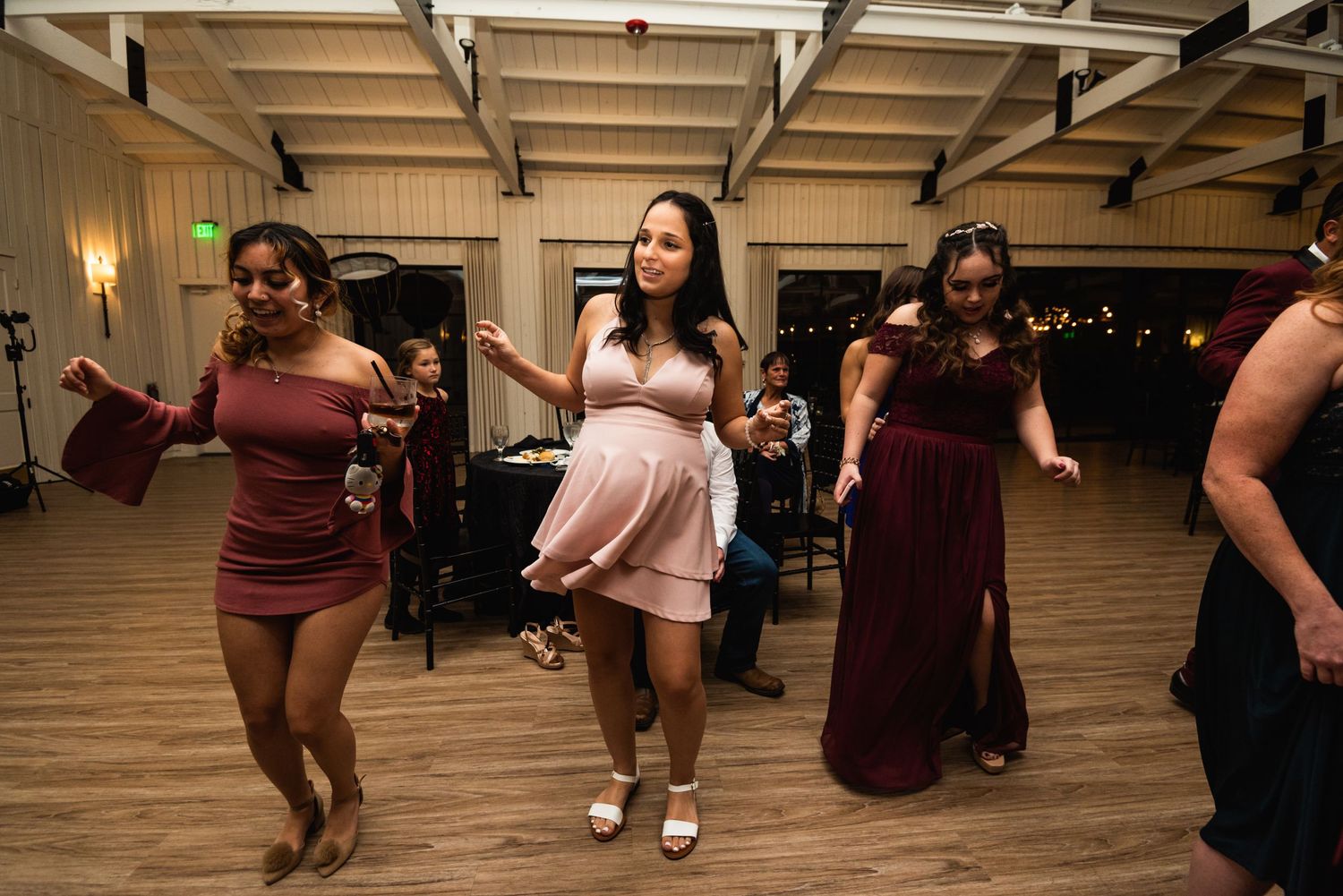 Guests in burgundy and pink dresses dancing together at a wedding reception.