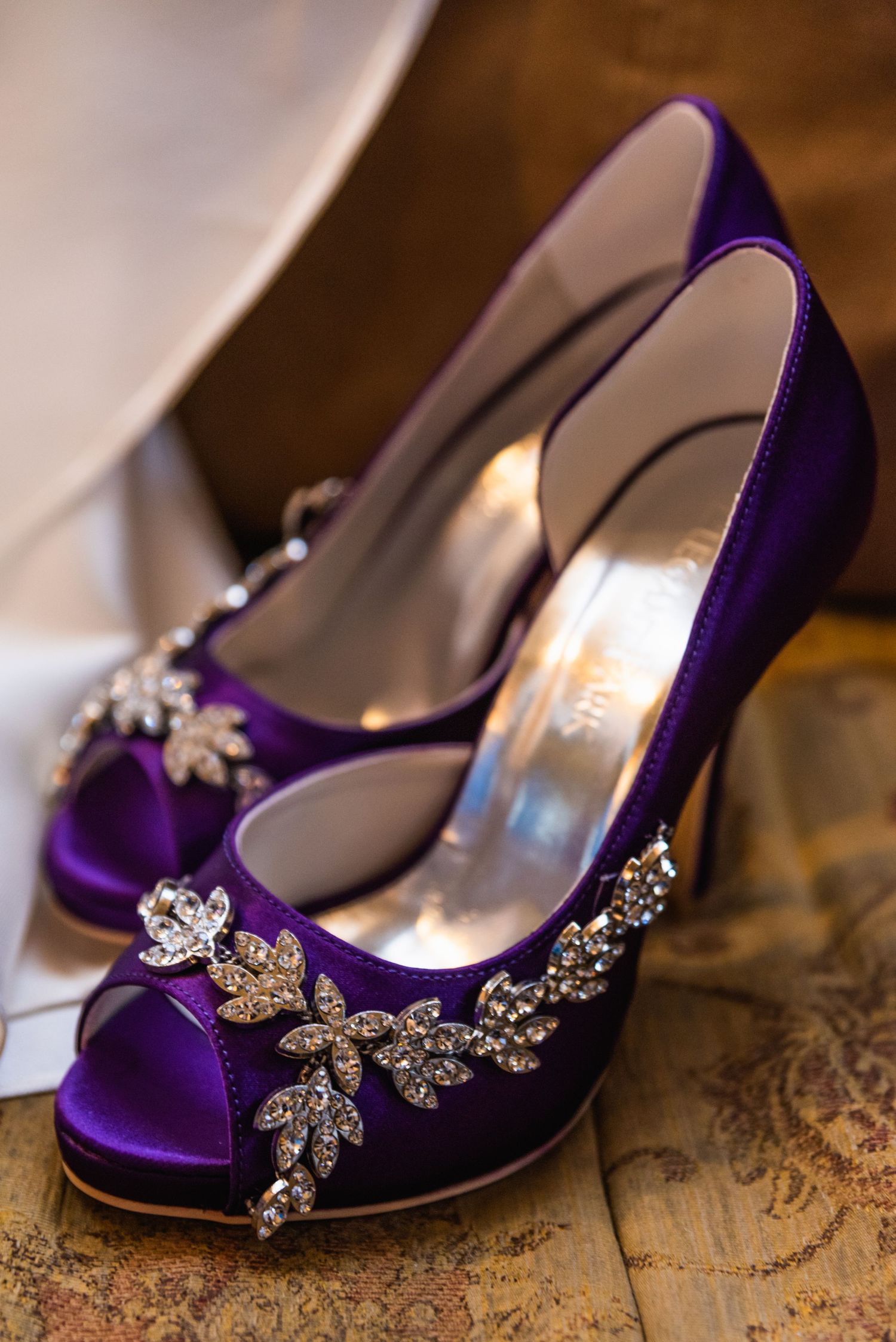 Purple satin wedding shoes with crystal embellishments displayed on vintage surface.