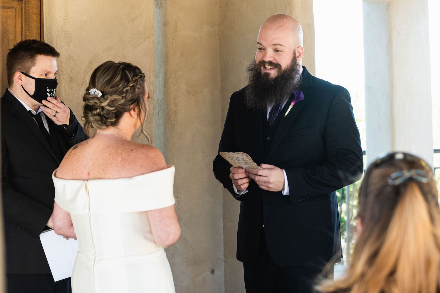 Outdoor wedding ceremony with officiant reading from papers while guests observe.