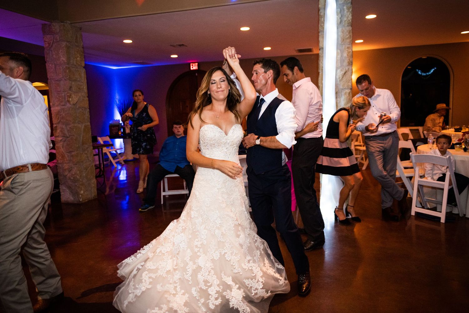 Newlyweds share their first dance in an elegantly lit reception venue with purple ambient lighting.
