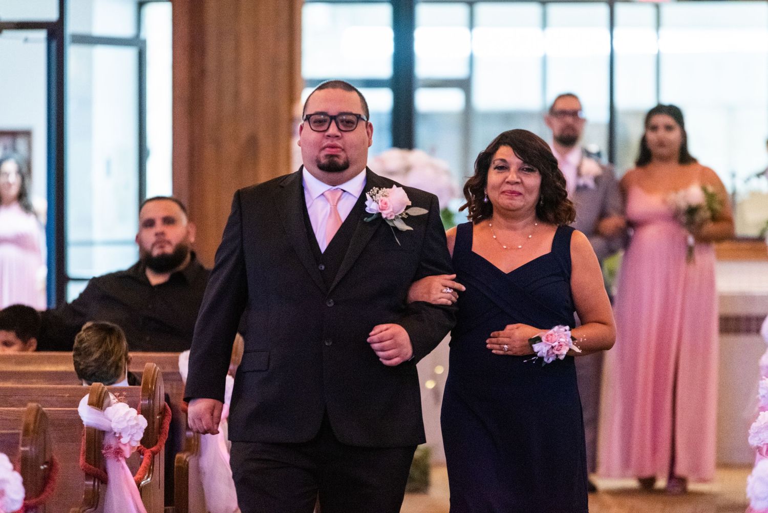 Wedding processional in church with attendants in pink dresses.