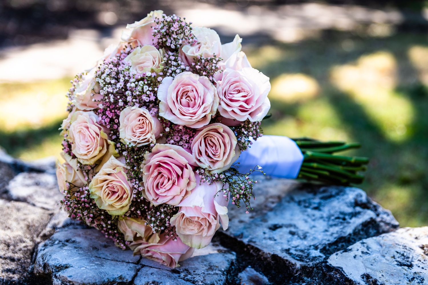 A romantic bouquet of pink roses resting on stone in natural sunlight.