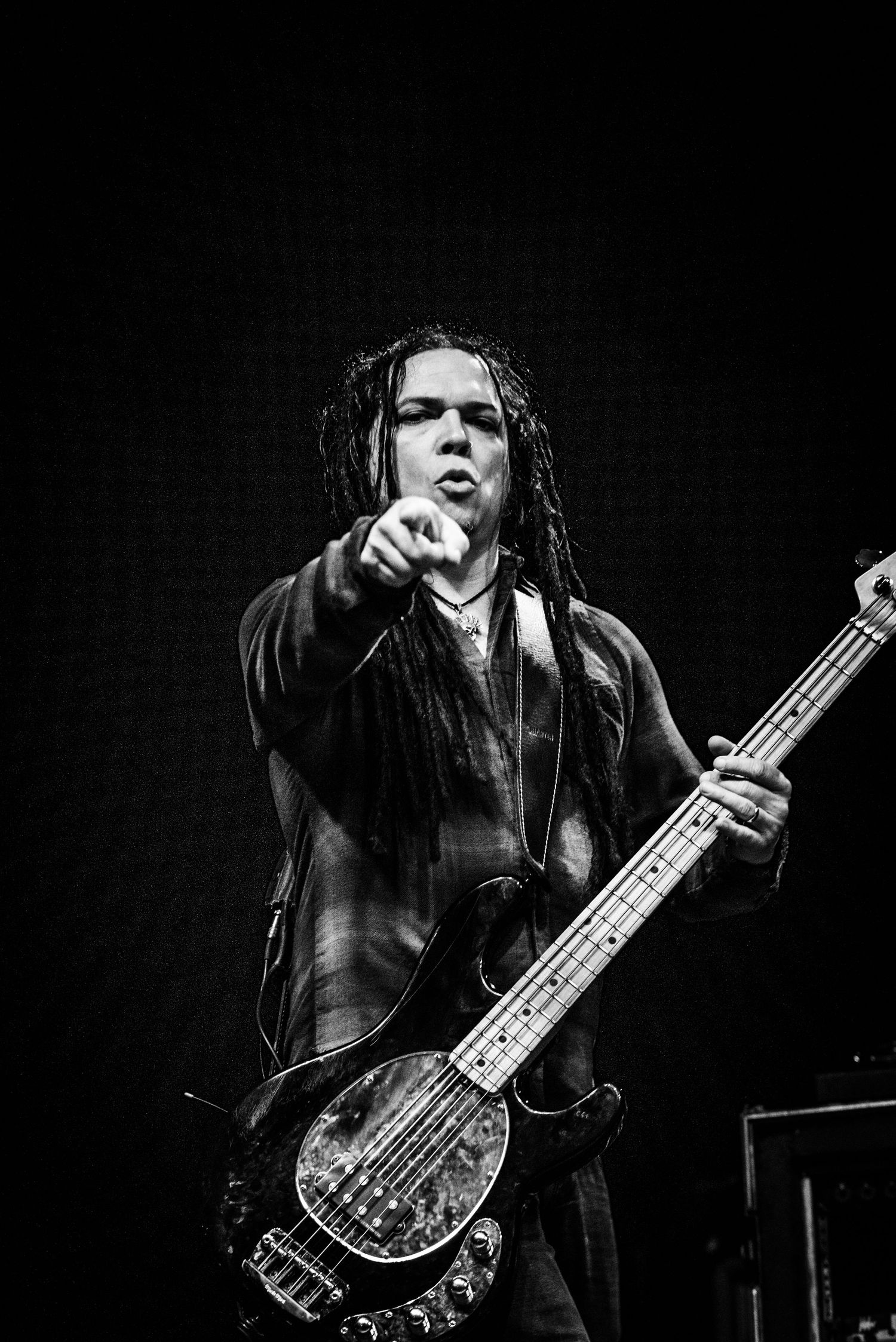 A black and white portrait of a bassist with dreadlocks pointing during a performance.