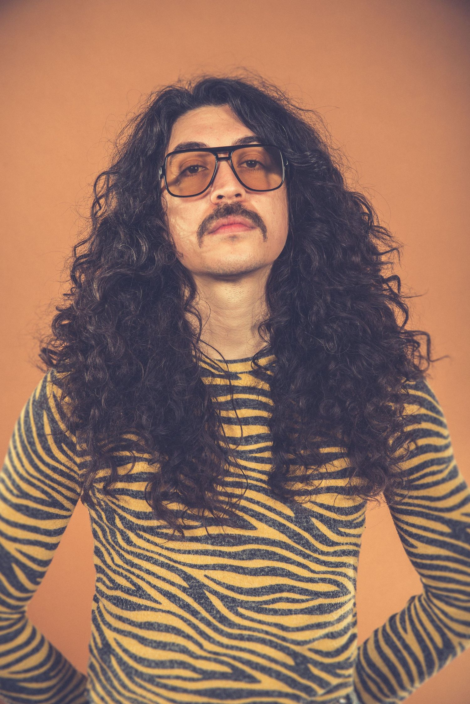 Vintage fashion portrait featuring tiger stripe shirt and glasses against warm orange background.
