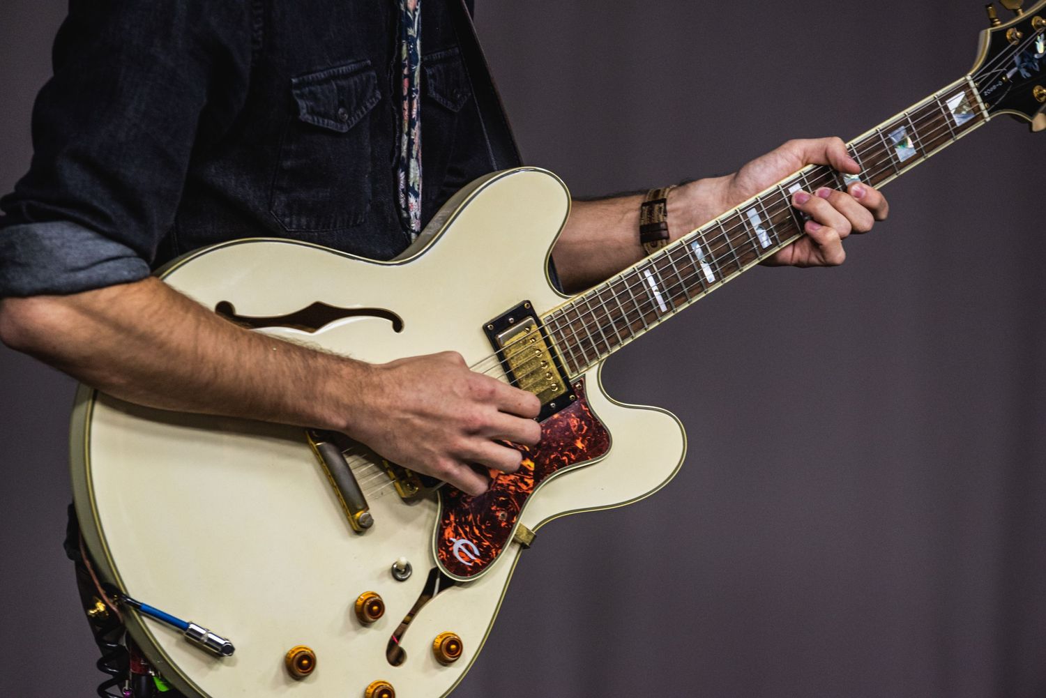 Close-up shot of hands playing a cream-colored hollow body electric guitar against dark background.