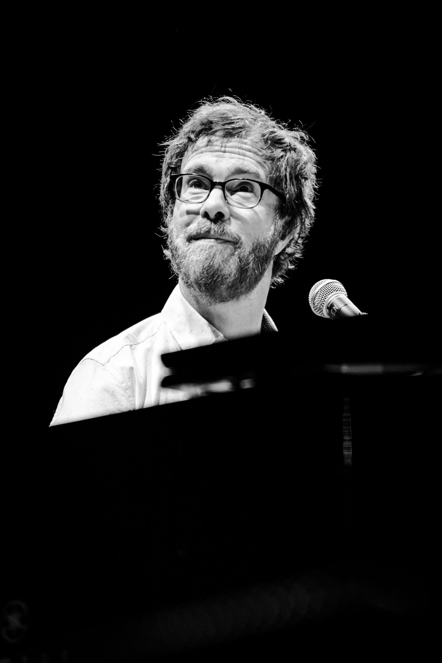 Black and white portrait of bearded pianist at grand piano during performance.