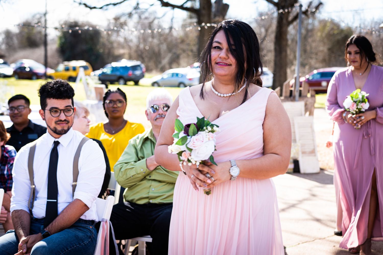 Wedding party members in pink dresses and formal attire gathered outdoors.