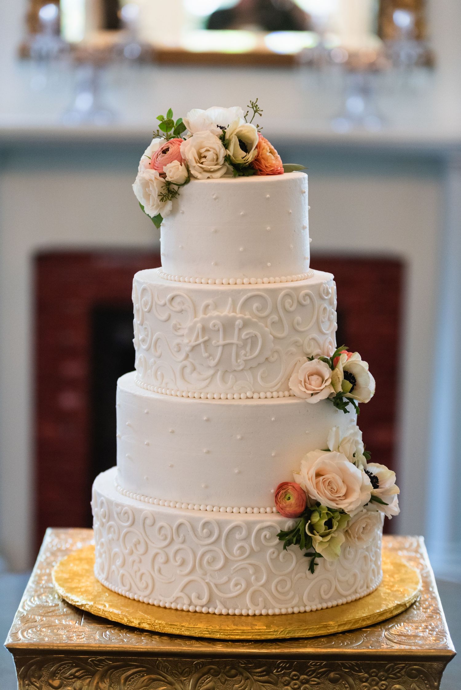 Elegant four-tier white wedding cake decorated with blush roses and intricate scroll piping.