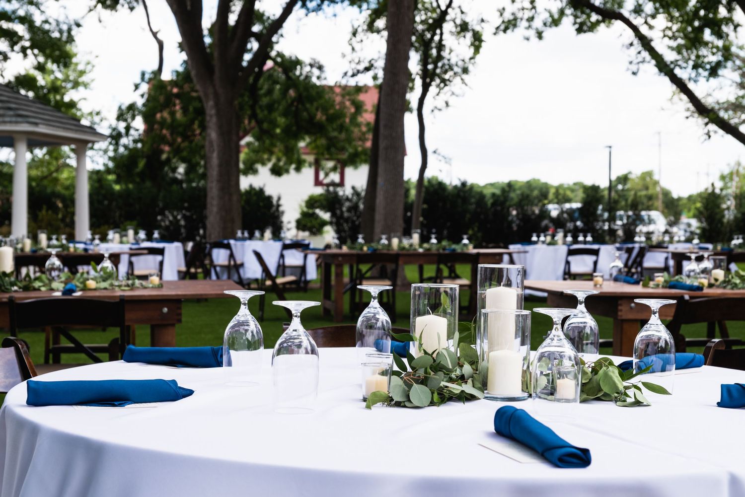 Outdoor wedding reception tables with white linens, navy napkins and greenery centerpieces.