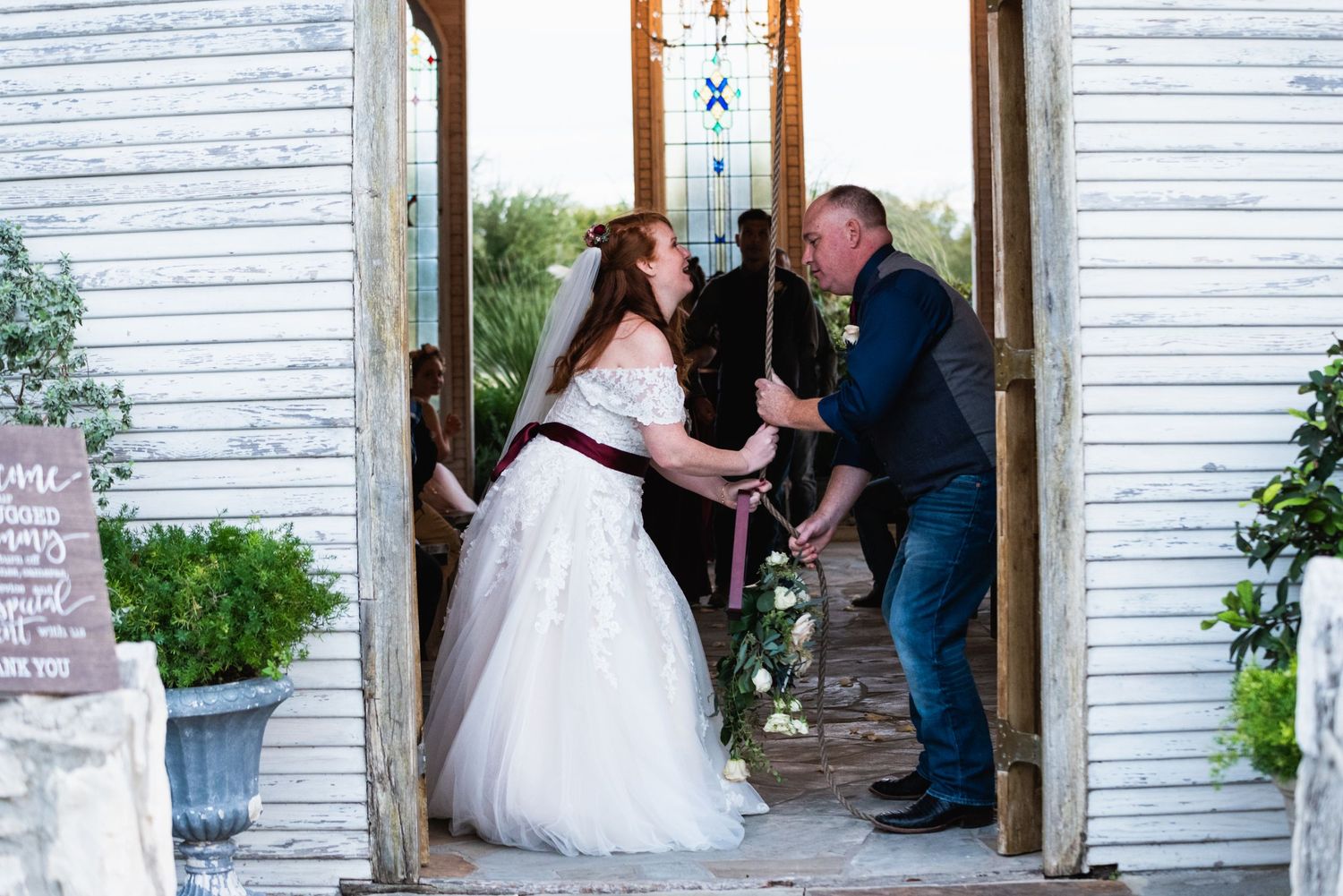 A couple sharing a playful moment in the doorway of a white chapel with stained glass windows.