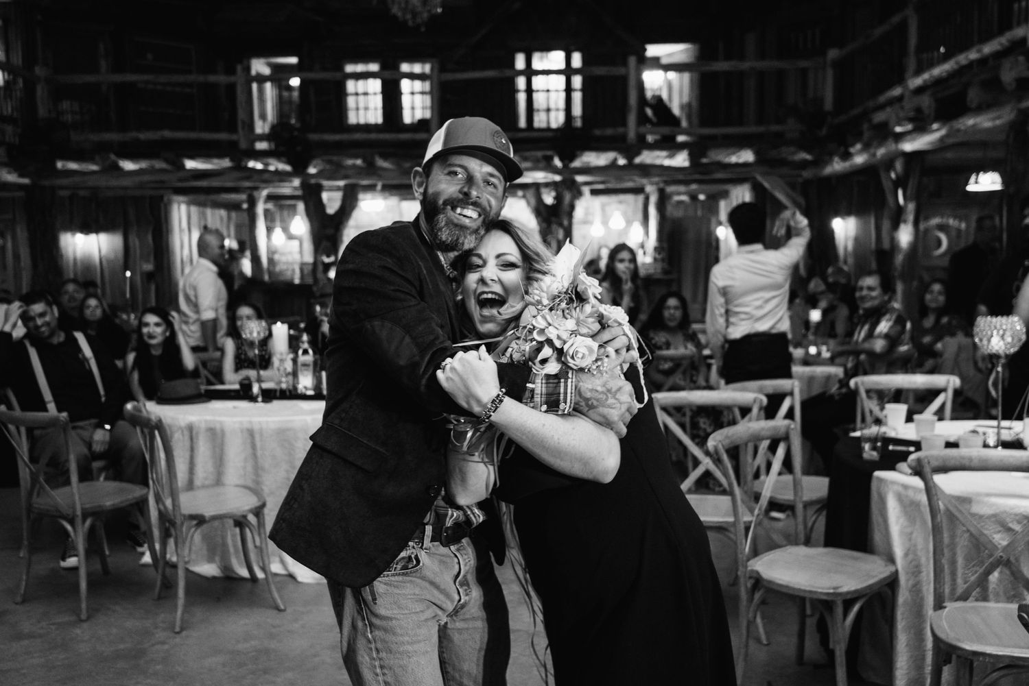 Black and white candid photo of guests sharing a lively moment at a wedding reception.