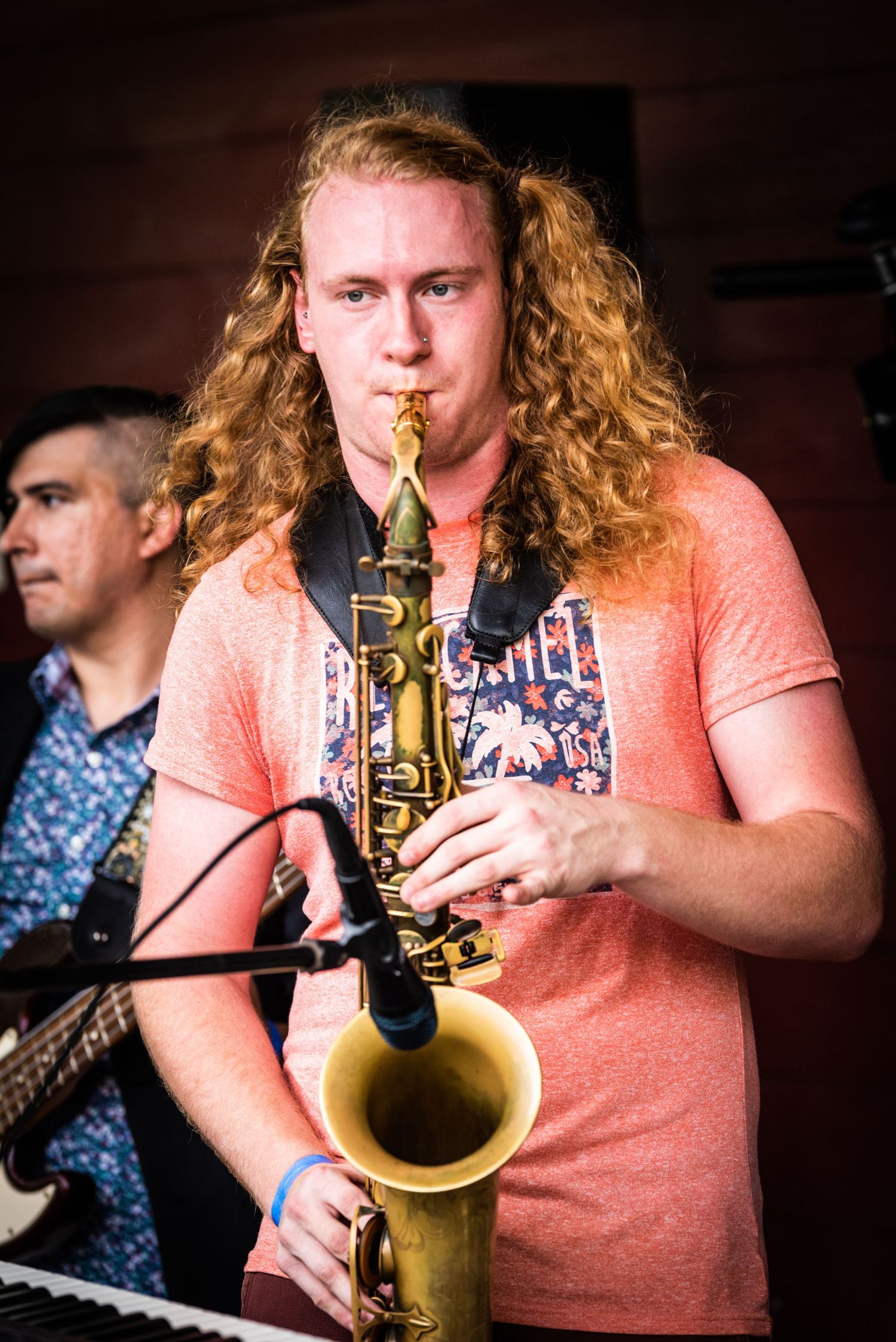 Saxophone player performing on stage in coral colored shirt.