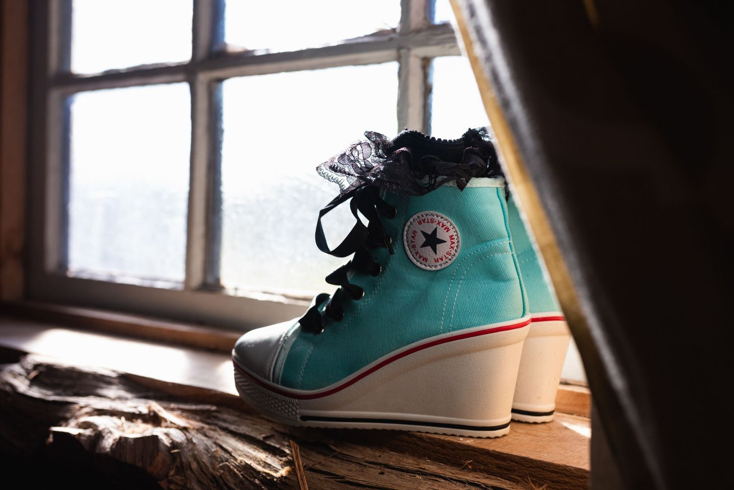 A teal Converse wedge sneaker sitting on a weathered windowsill in dramatic lighting.