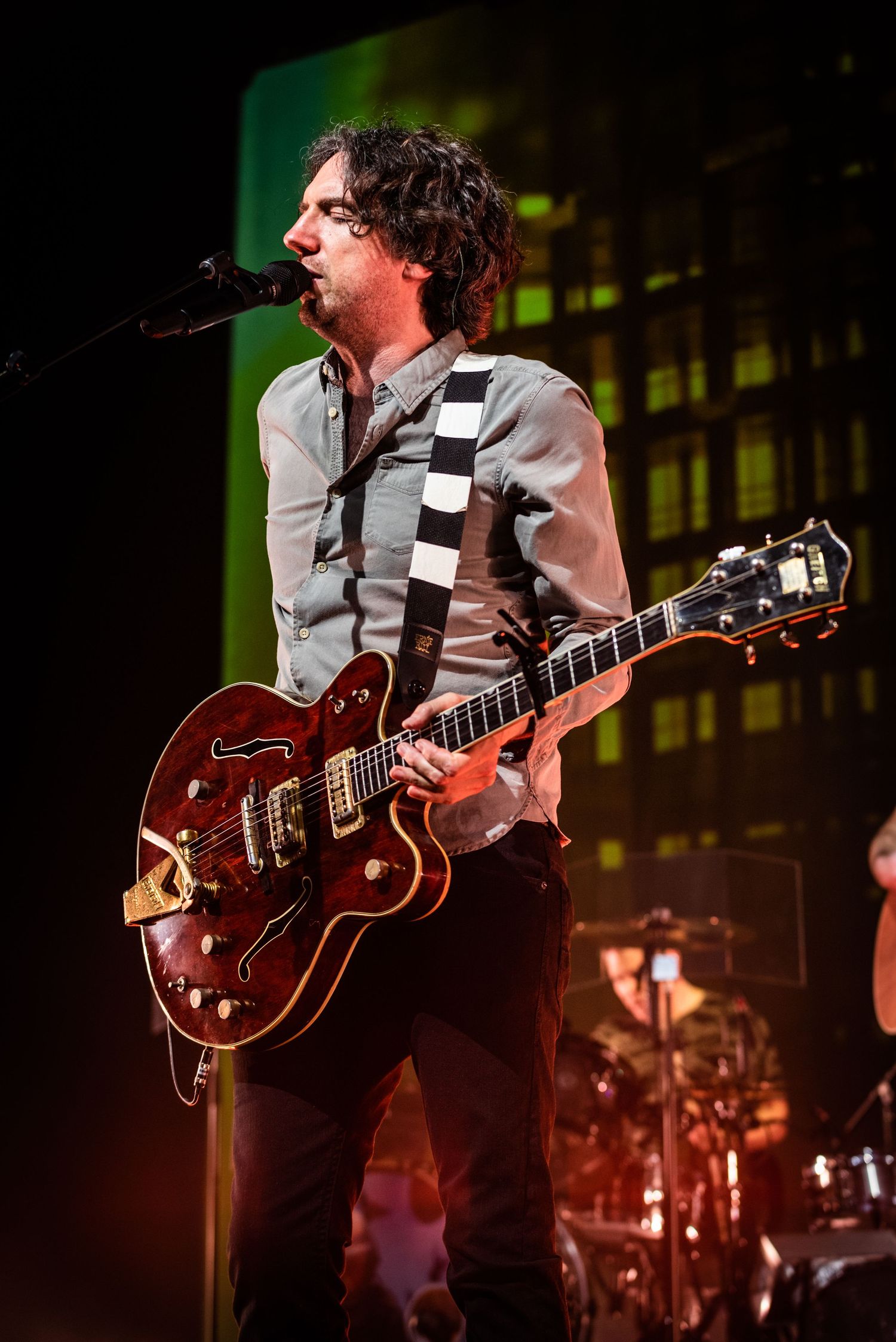 Guitarist plays red Gretsch hollow body electric guitar while performing on illuminated concert stage.