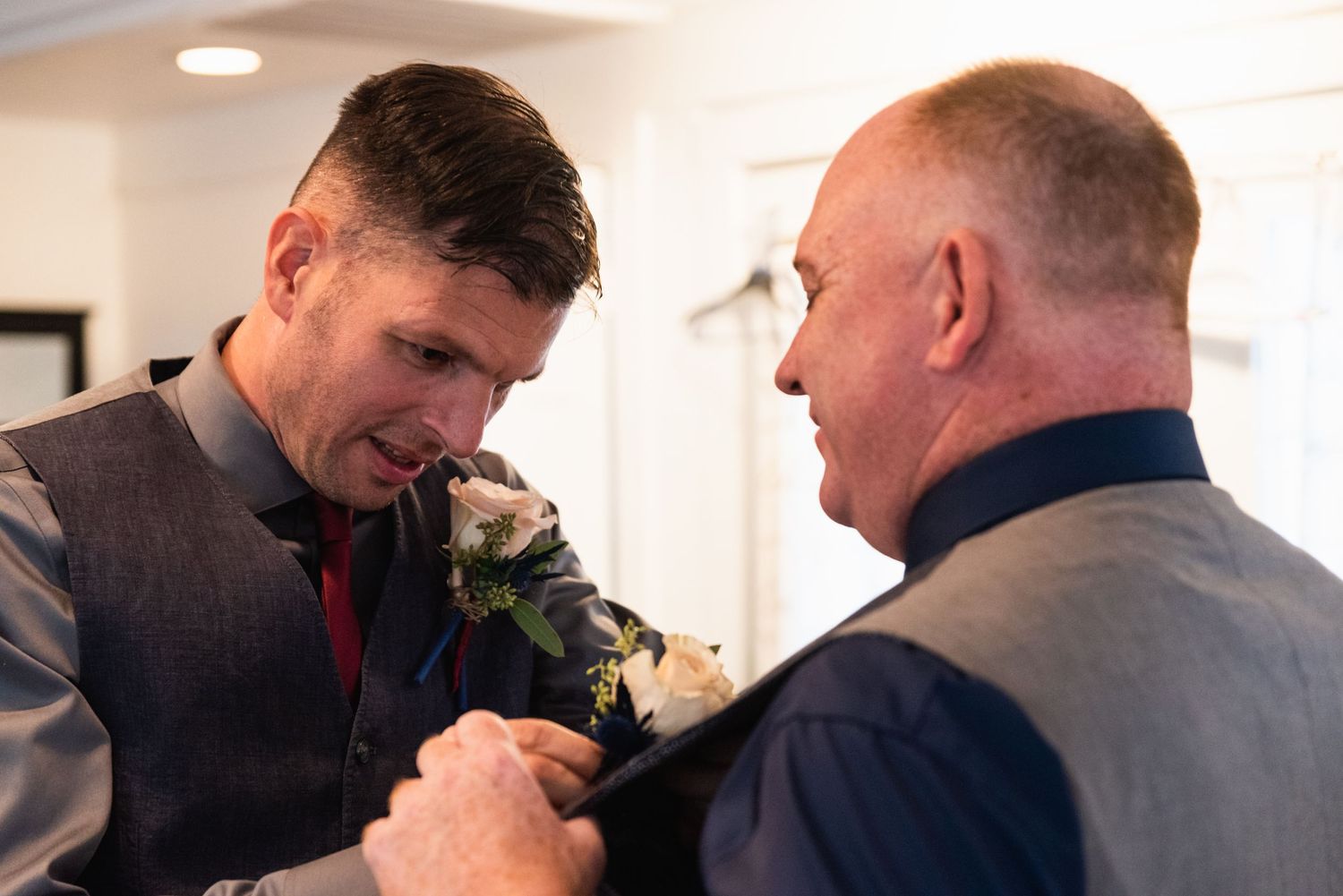 Two men share a candid moment while adjusting their formal wear.