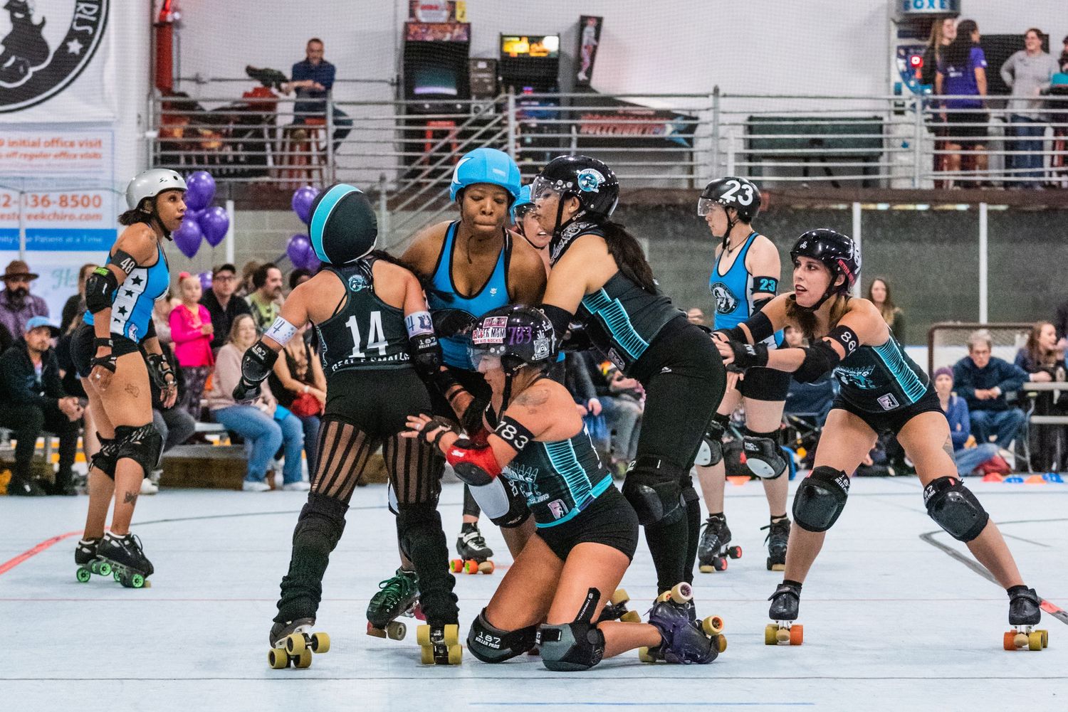 Roller derby players form strategic formation during competitive match on indoor rink.