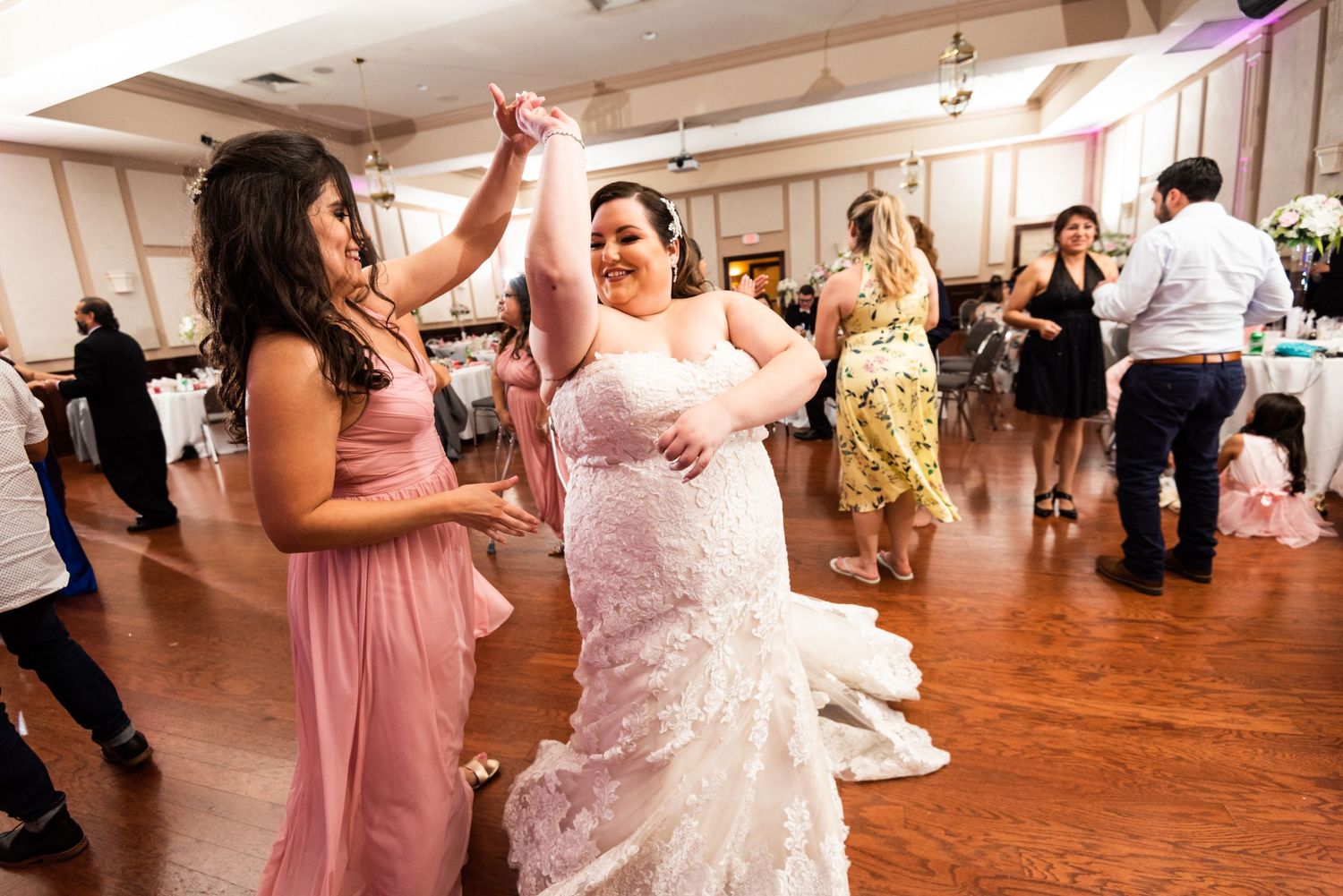 Party guests dancing and celebrating on wooden dance floor at wedding reception.