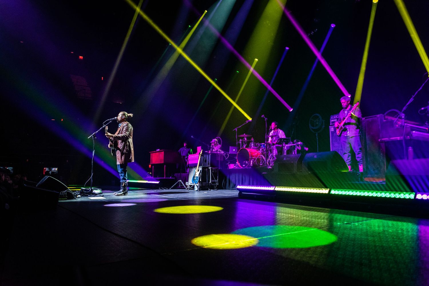 Band performing on concert stage with colorful lighting effects and spotlights.