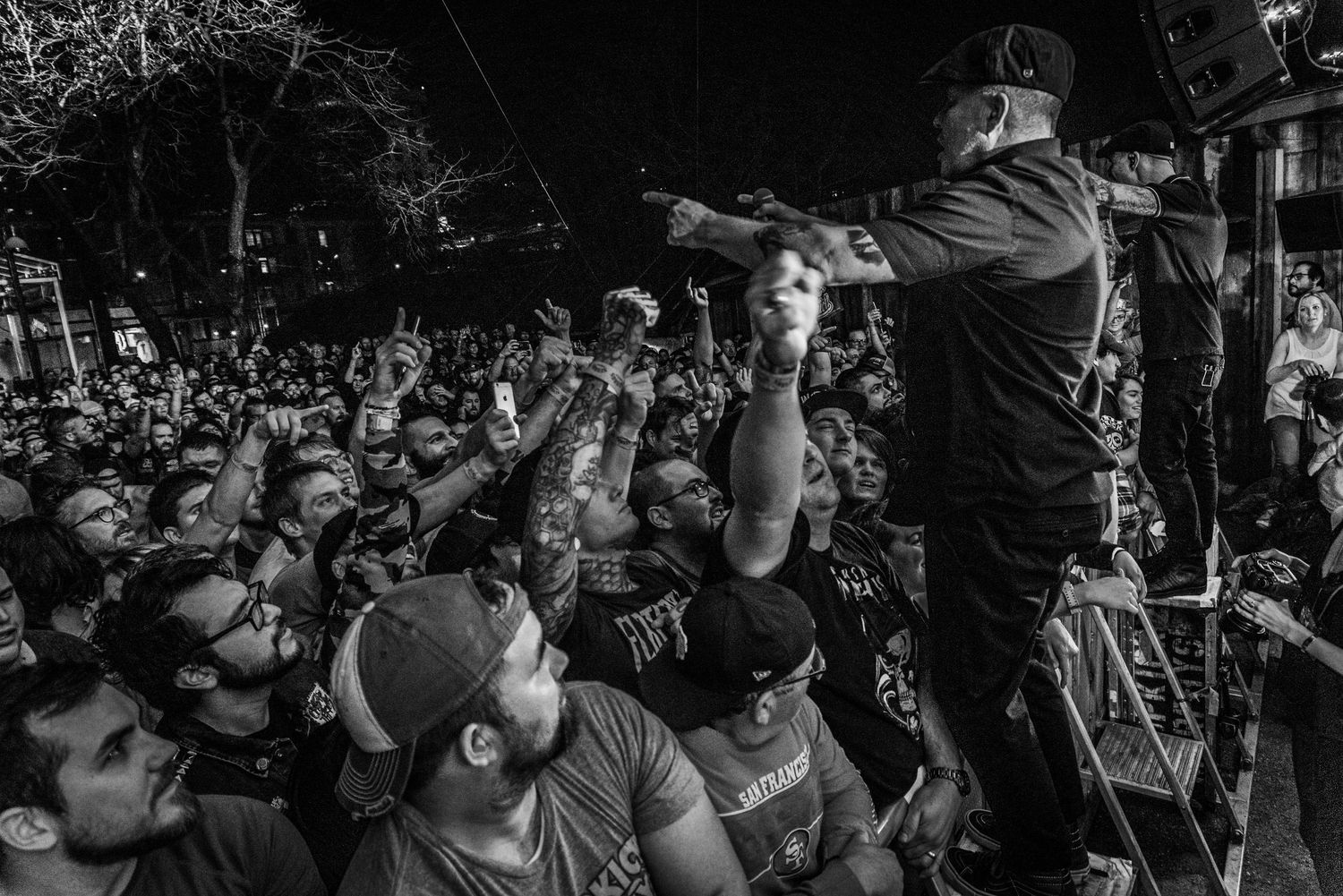 Black and white wide shot of performer engaging with large crowd from elevated stage position.