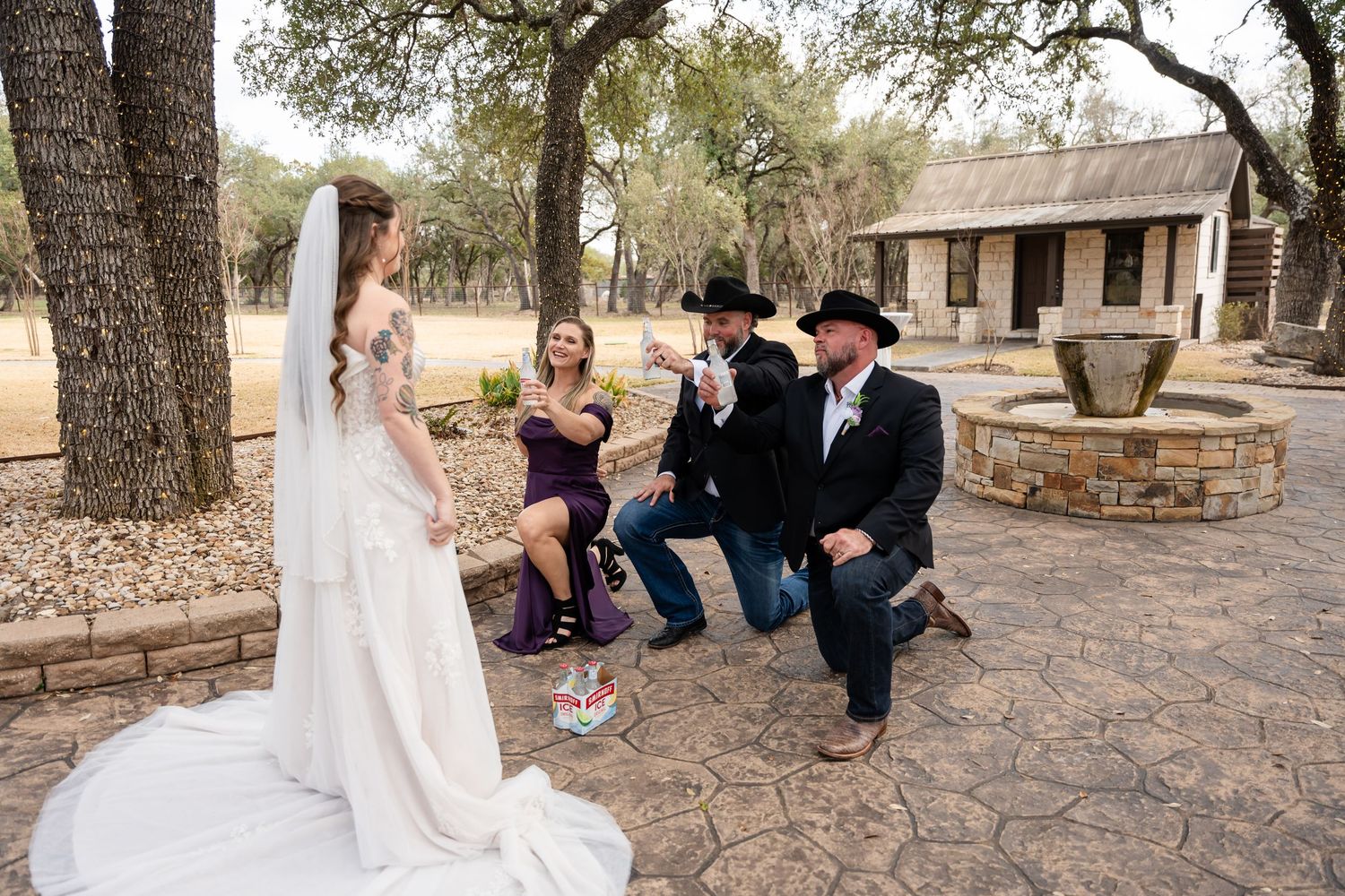 Bride in white gown with wedding party in cowboy hats celebrating outdoors at rustic Texas wedding venue.