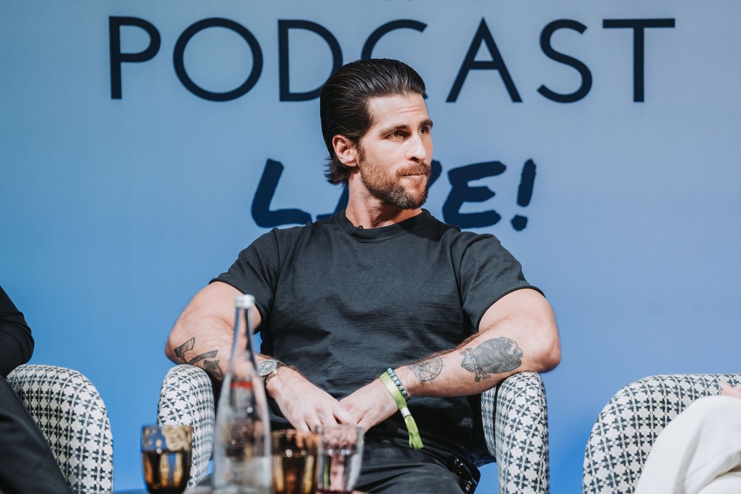 A podcast host in a black t-shirt sits in front of a microphone during a recording session.