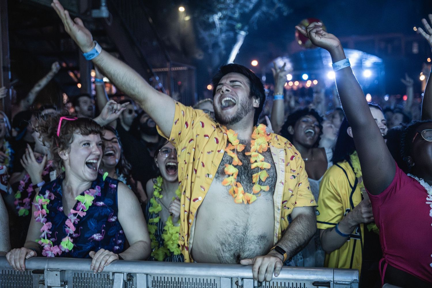 Energetic crowd of concert-goers dancing and cheering with raised arms at a nighttime music event.