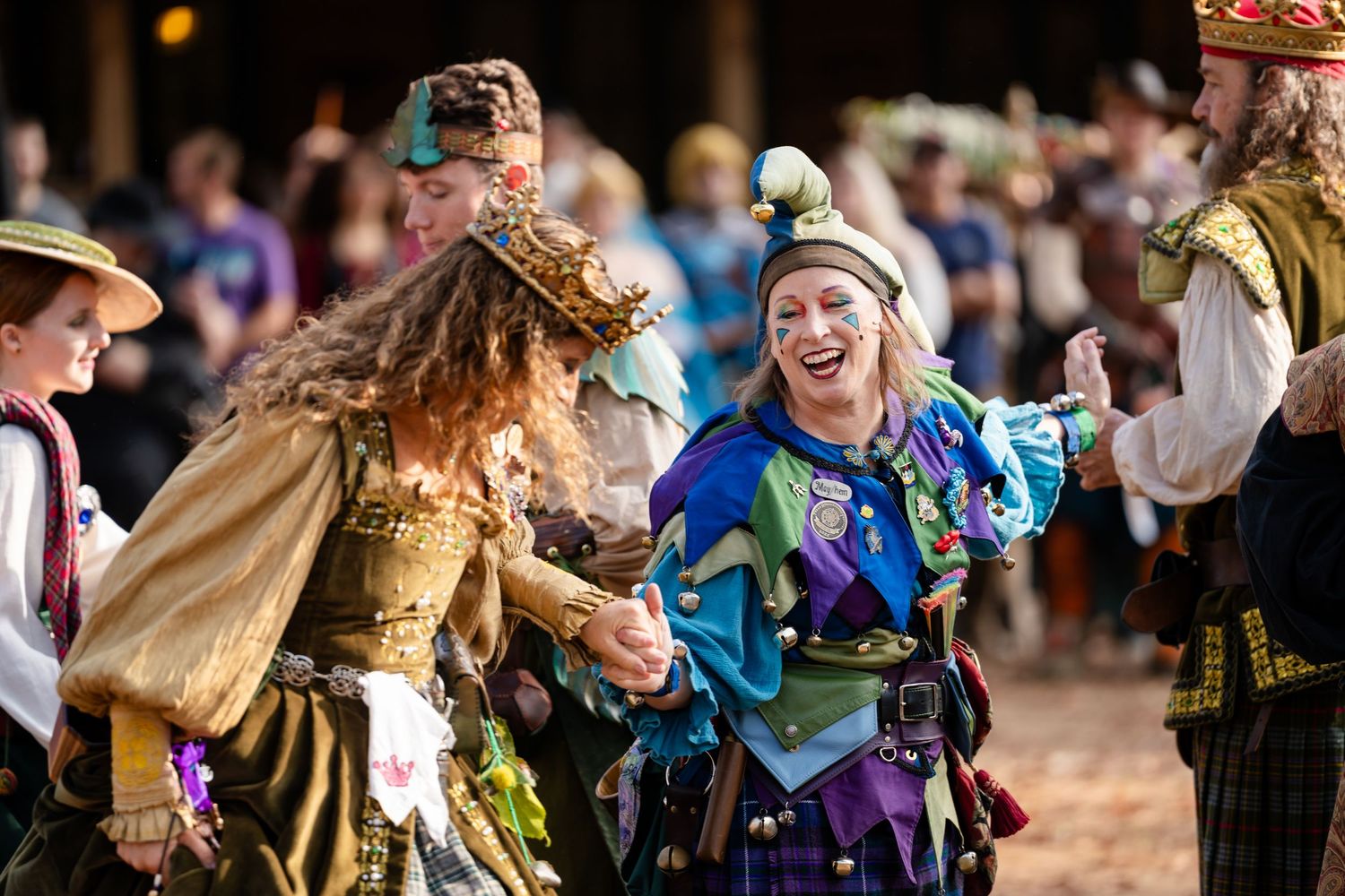 Performers in colorful medieval costumes dance and celebrate at a Renaissance festival.