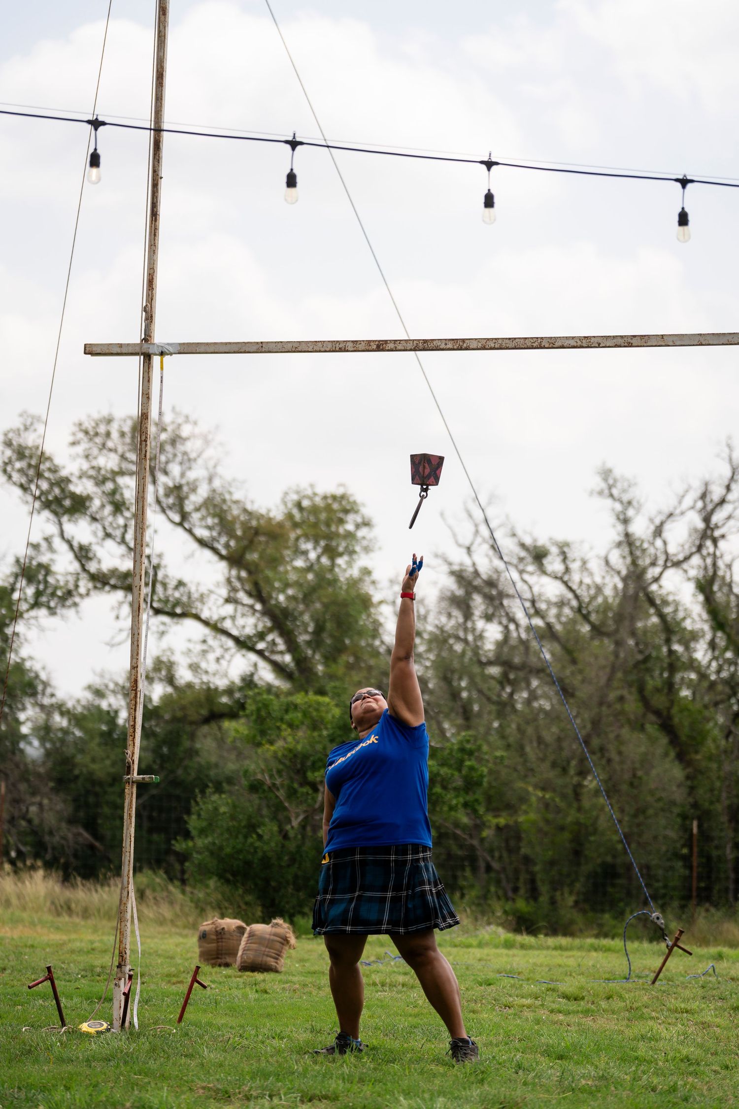 Person in a blue shirt swinging on a zip line across a grassy field with string lights overhead.