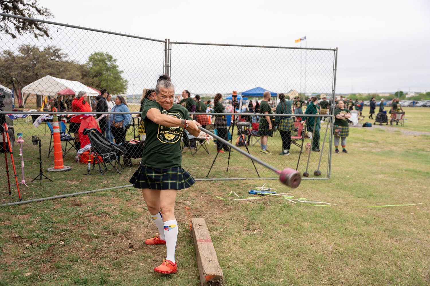 Woman in kilt competes in Highland Games hammer throw event at outdoor festival.