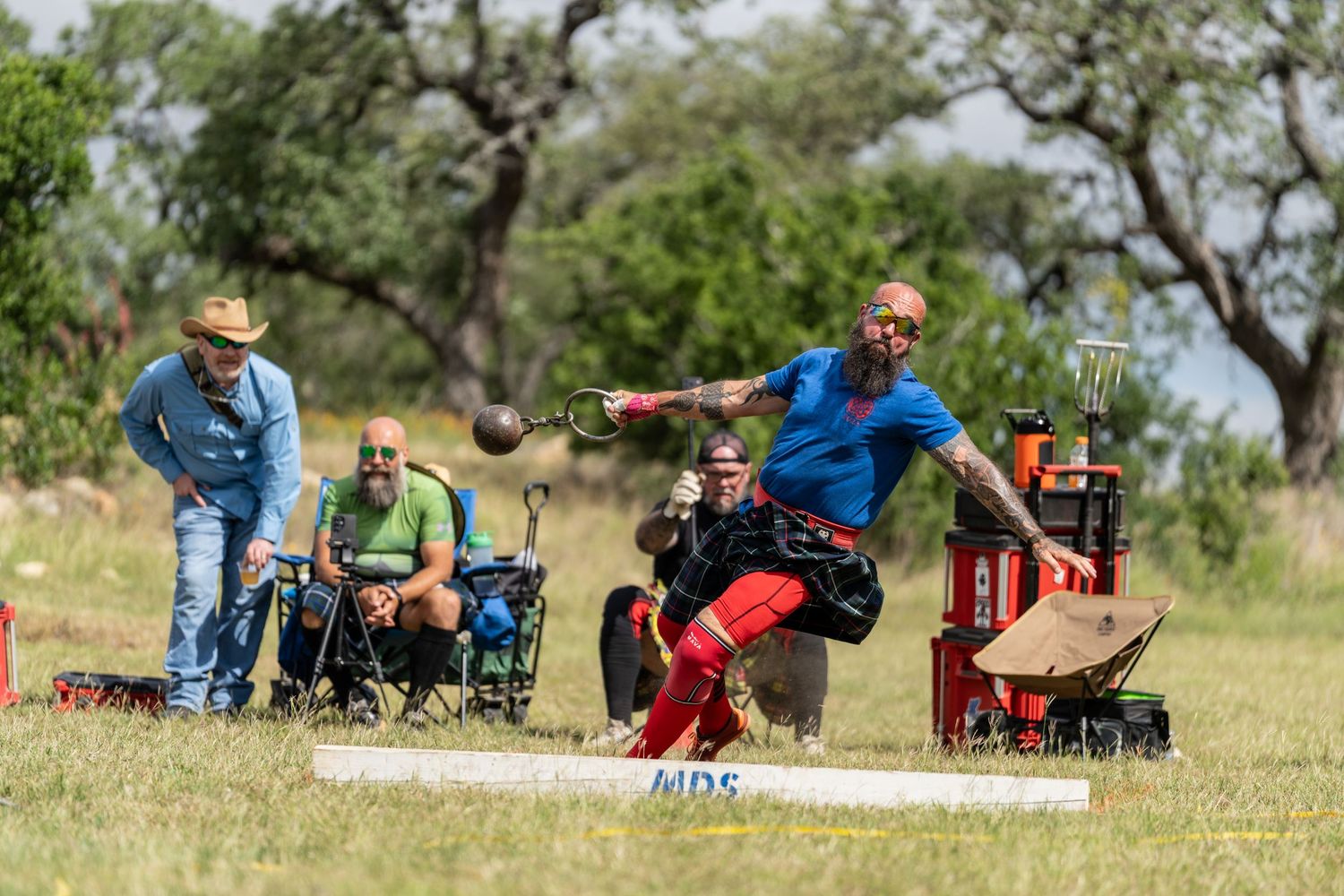 Athlete competes in outdoor disc golf tournament, releasing disc mid-throw while spectators watch on a sunny day.