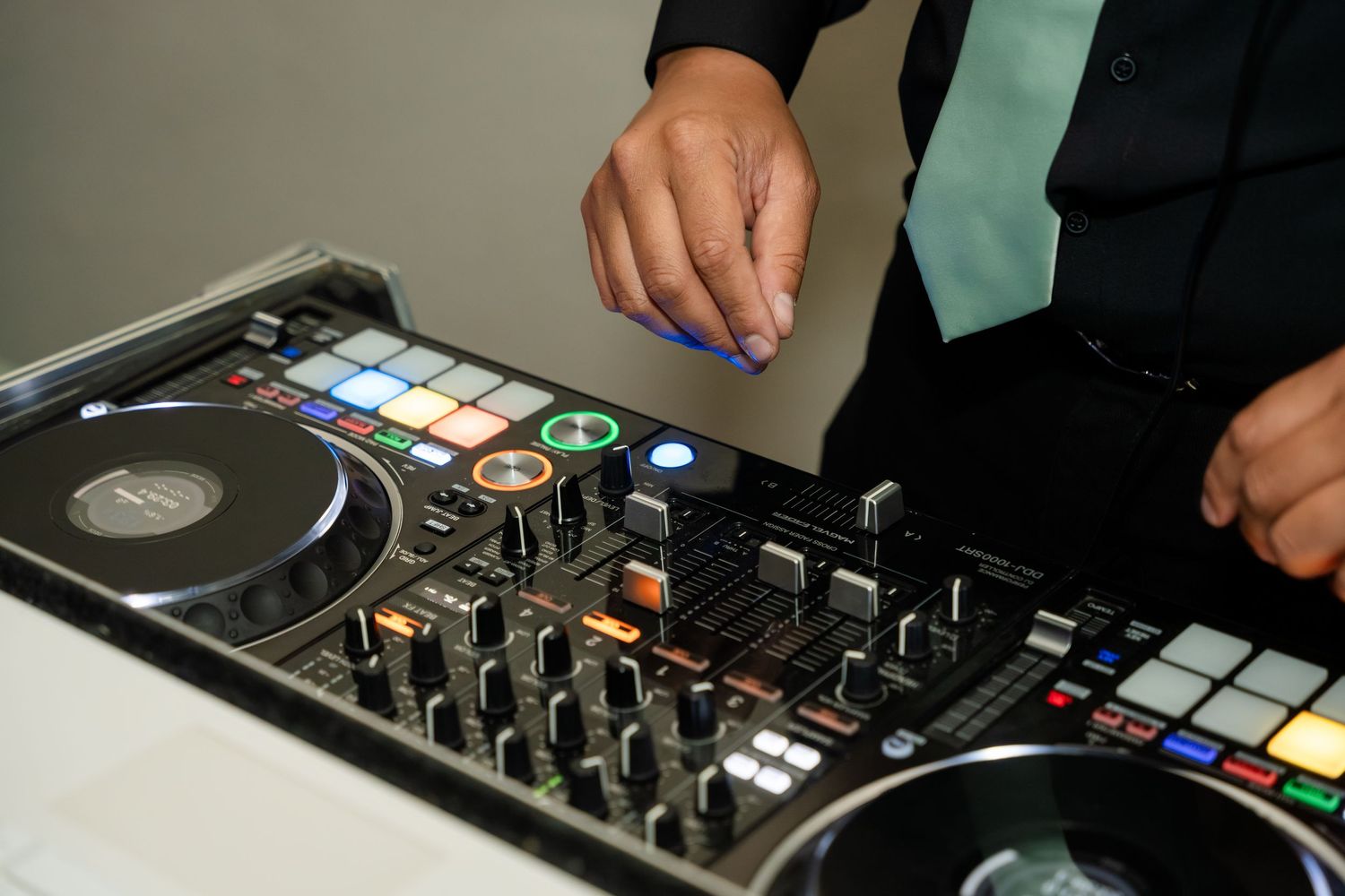 DJ mixing music on a professional turntable controller with colorful buttons at an event.