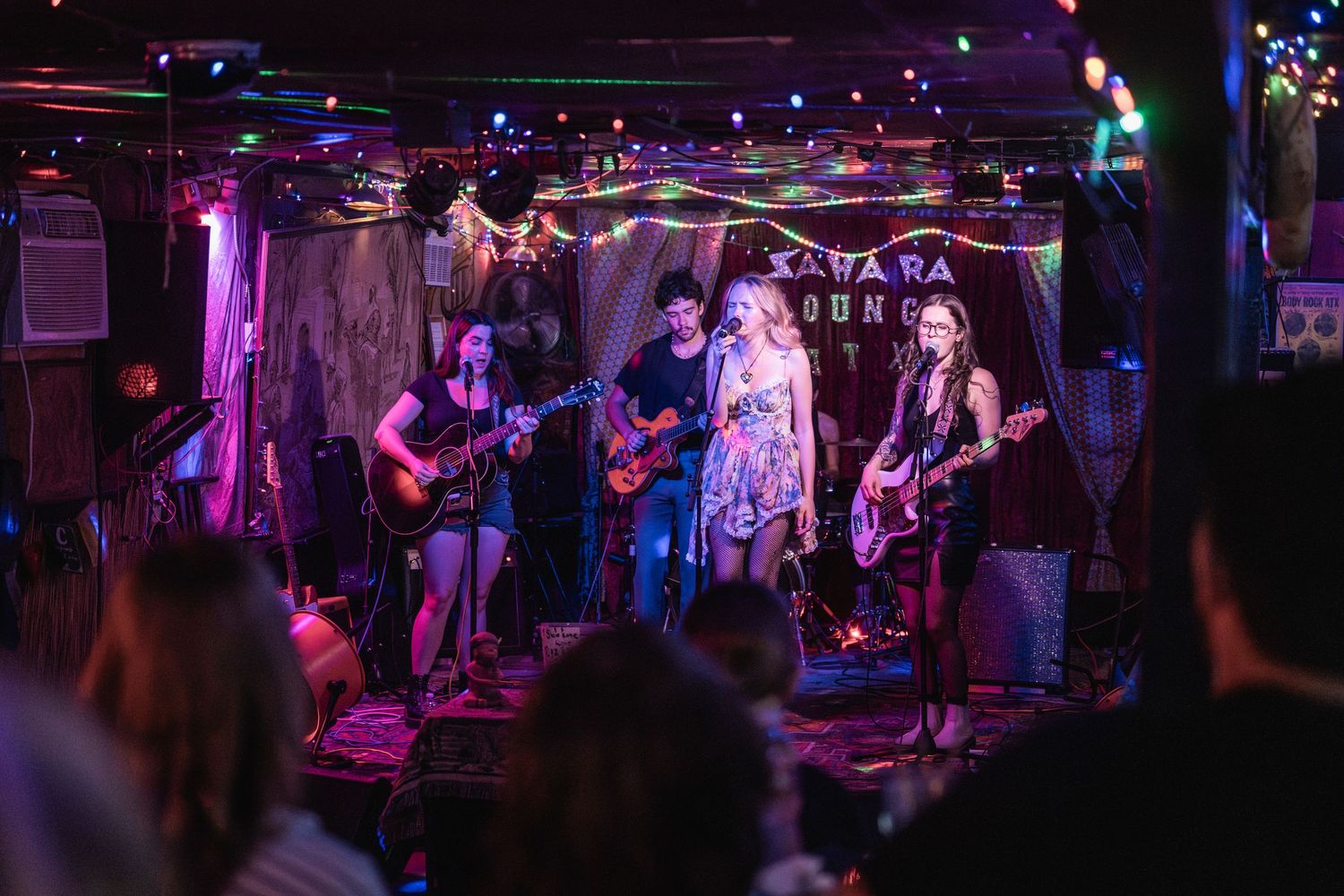 A rock band performs on stage in a dimly lit venue with purple and blue lighting creating an energetic atmosphere.