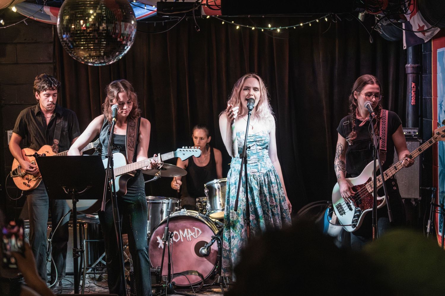 Live band performs on stage with guitars and drums under moody lighting at a music venue.
