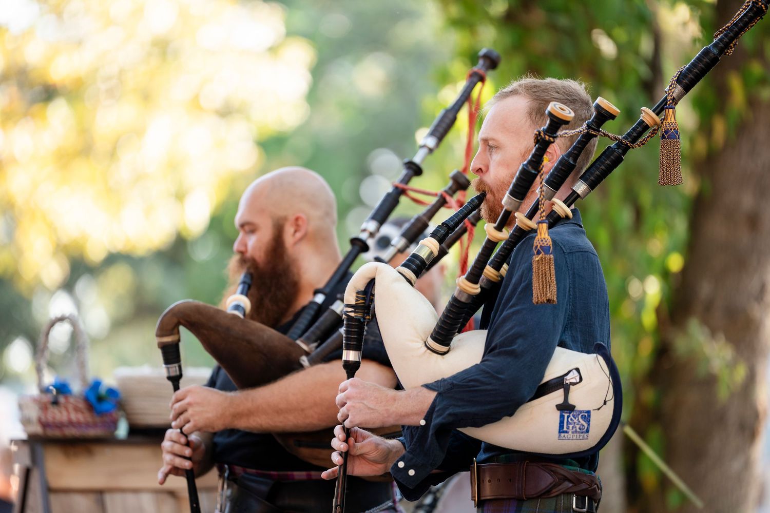 Musicians in kilts perform traditional Scottish bagpipe music outdoors at a cultural event.