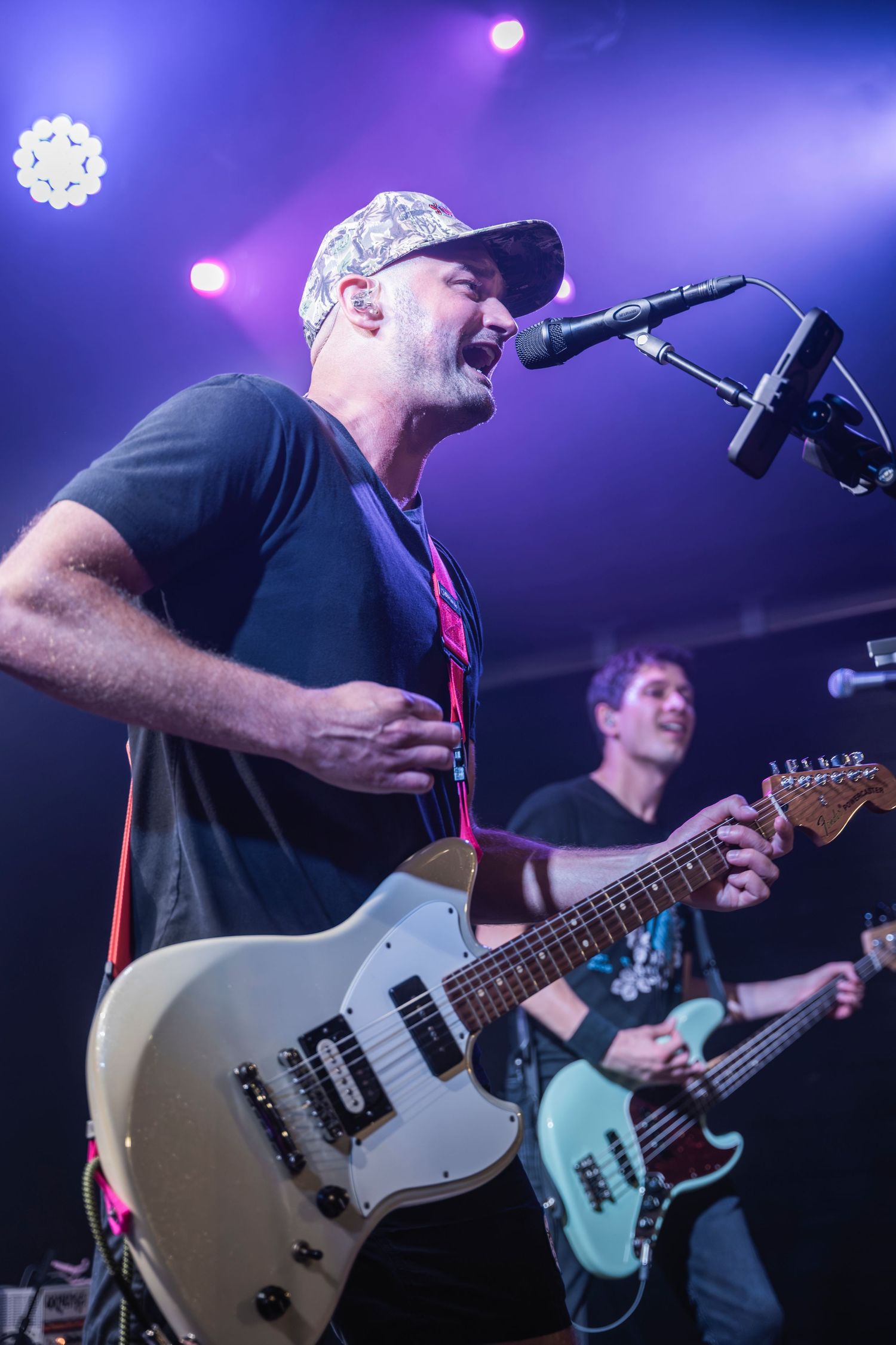 Musician performs on stage with a light colored electric guitar under blue and purple stage lighting.