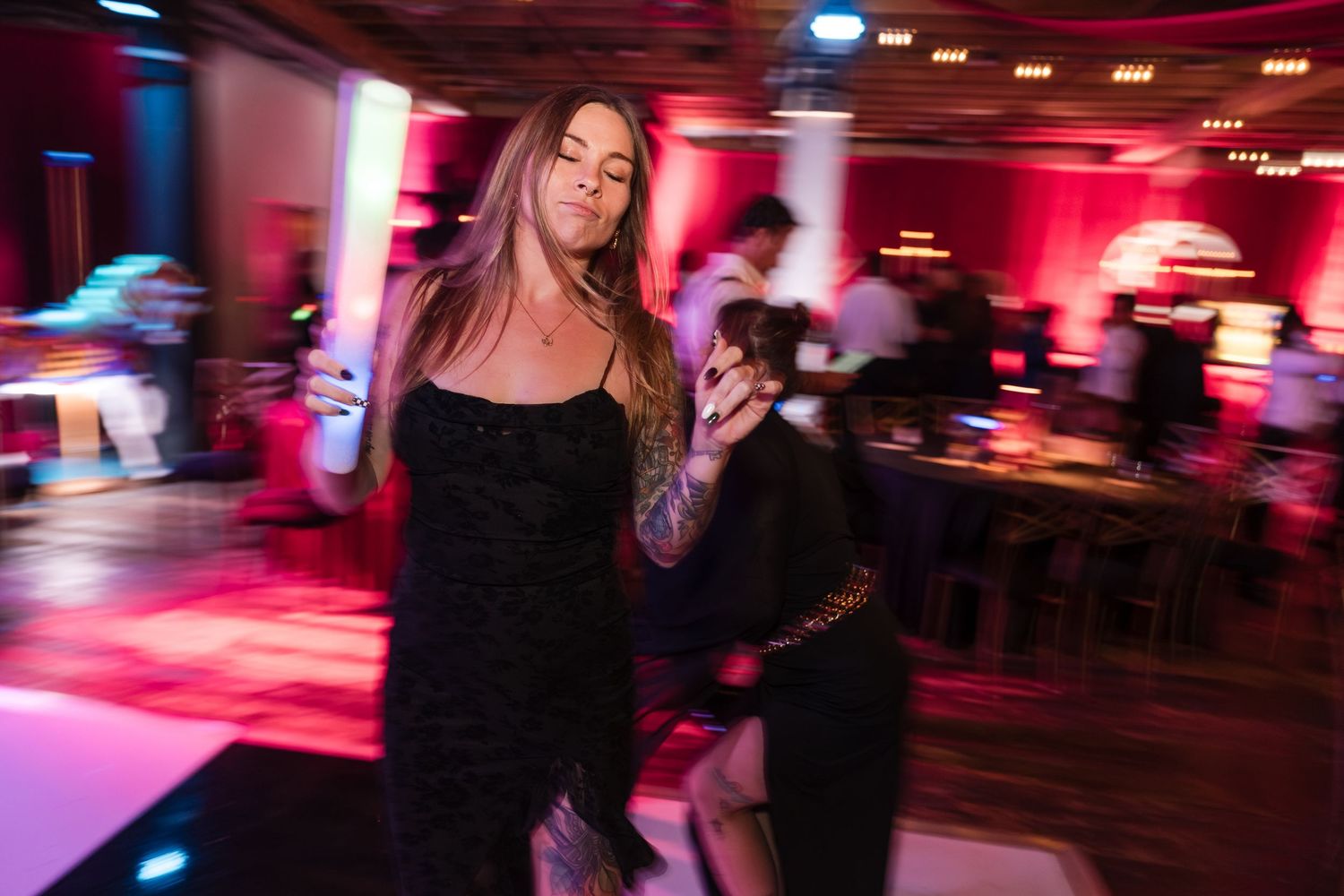 A nightclub scene with red and pink lighting illuminates dancers on a crowded dance floor.
