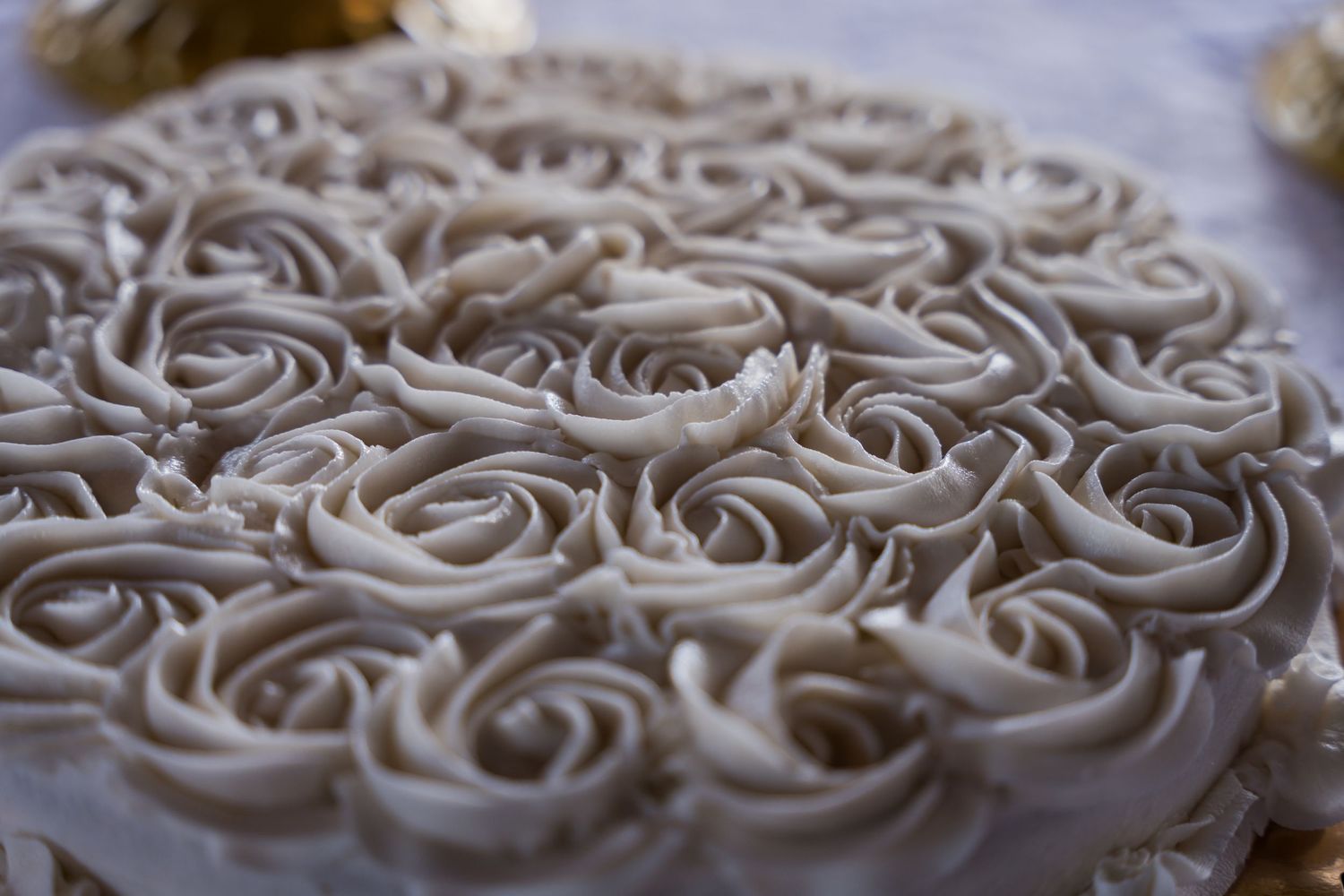 Close-up of intricate white buttercream frosting roses piped in a swirling pattern on a cake surface.