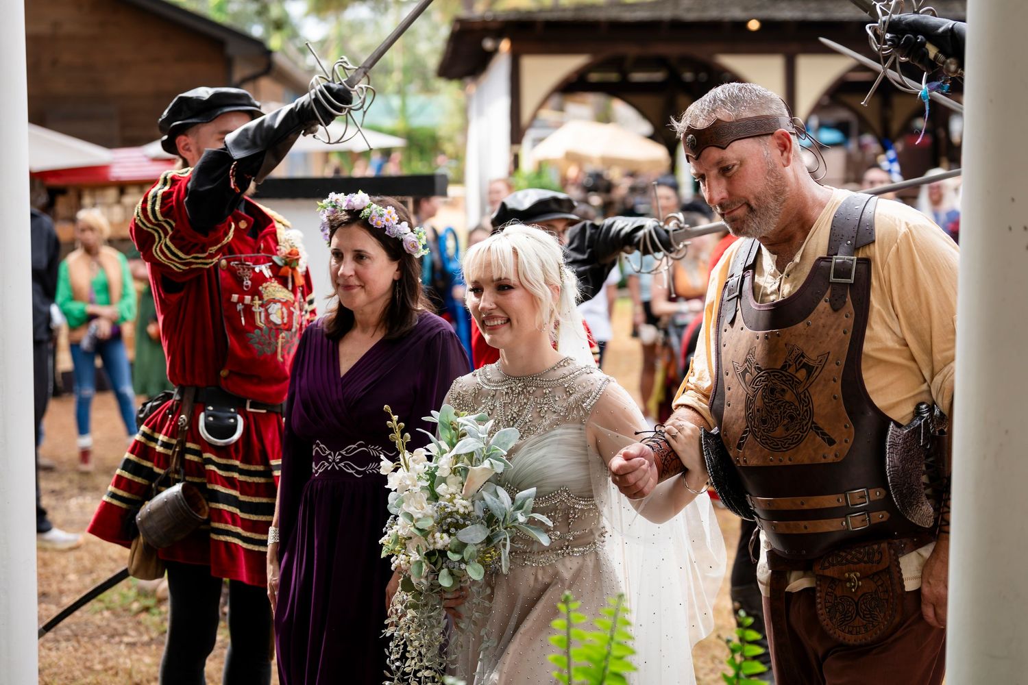 A couple celebrates at a Renaissance festival with costumed performers and attendees in period attire.