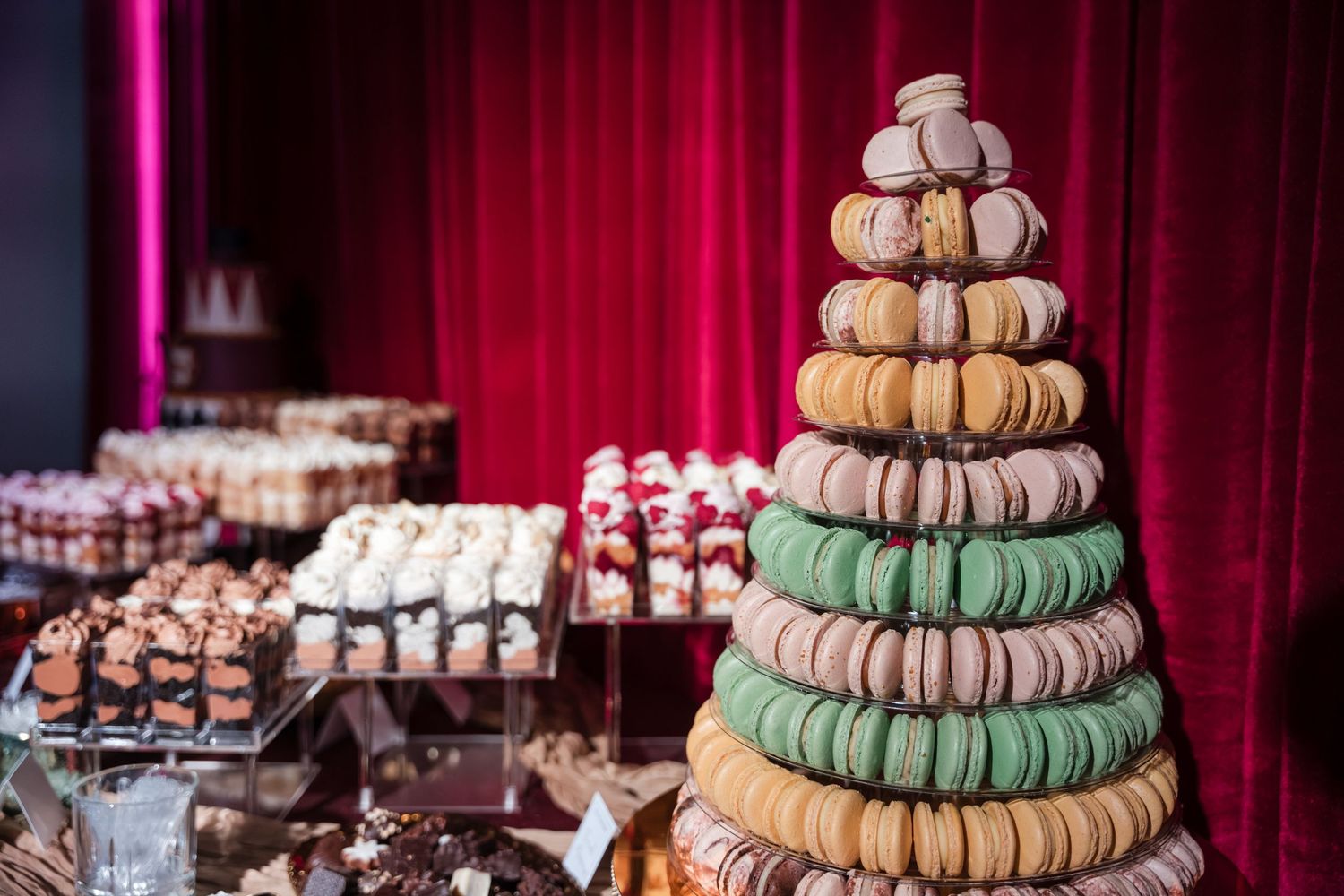 Colorful macarons arranged in a tower display with various flavors and colors against a red curtain backdrop.