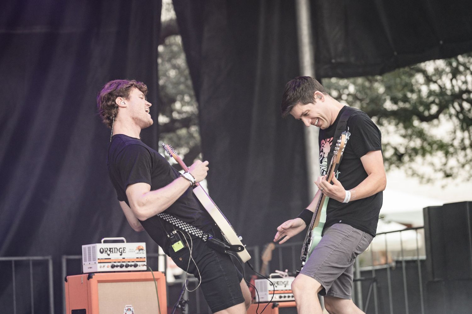 Two musicians perform energetically on stage with guitars and amplifiers during an outdoor concert performance.