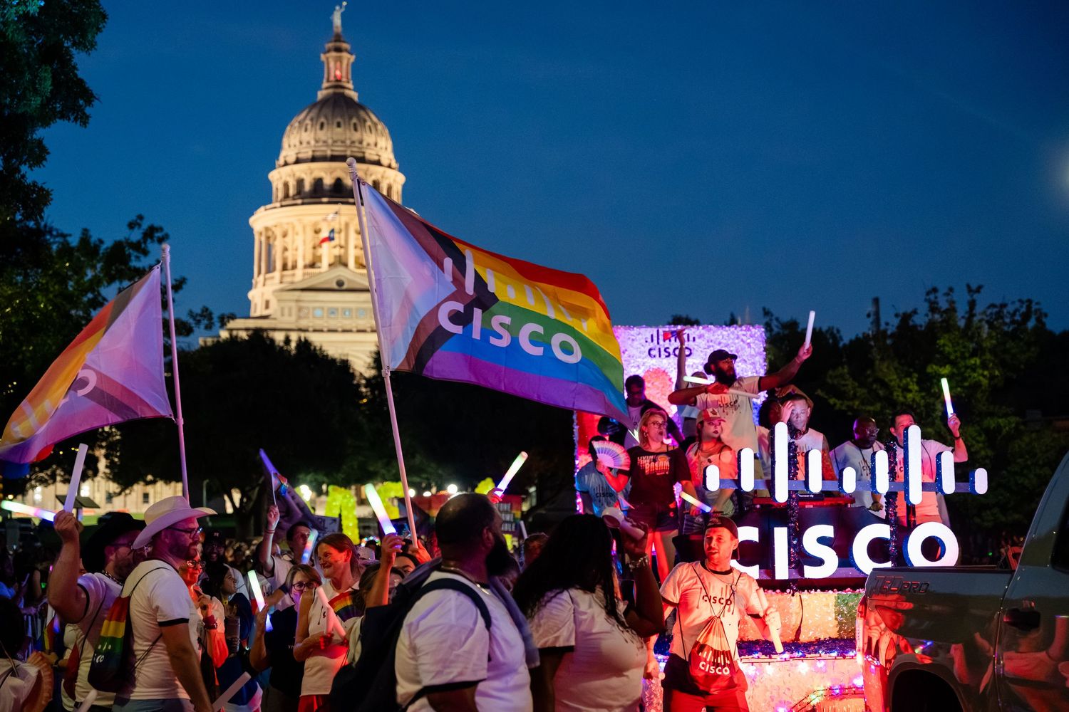 Cisco Pride parade float with rainbow flags near Texas State Capitol building at dusk.