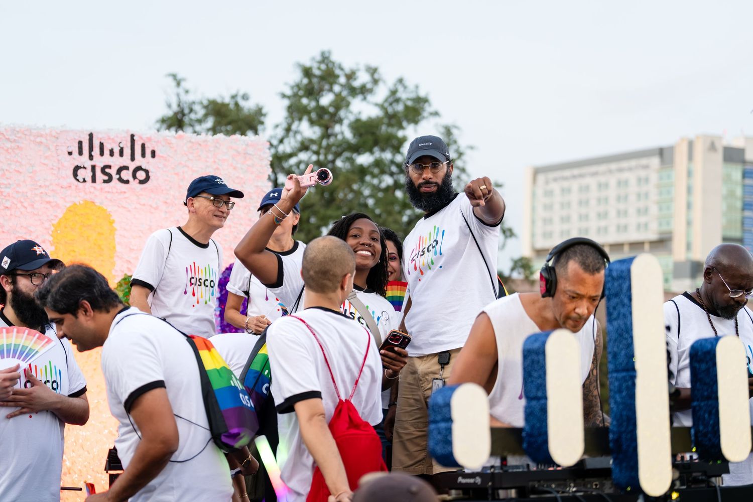 Cisco employees celebrate Pride parade, cheering on float with rainbow flags and branded shirts outdoors.