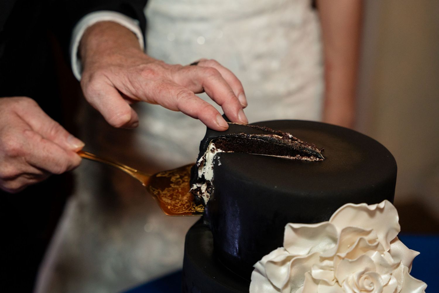 Close-up of hands cutting into a navy blue and white wedding cake.